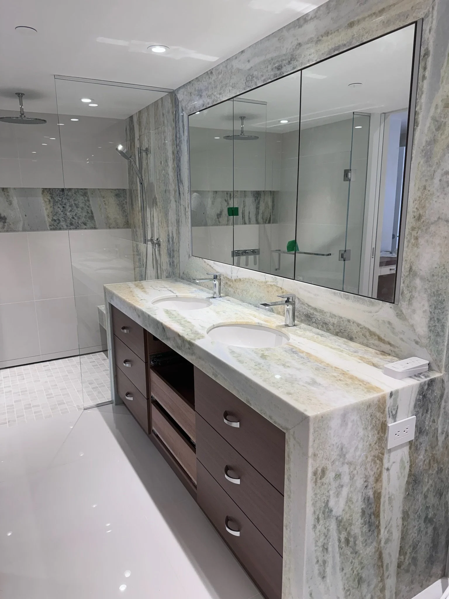Modern bathroom with double vanity, marble countertops, large mirror, and walk-in shower with glass enclosure.