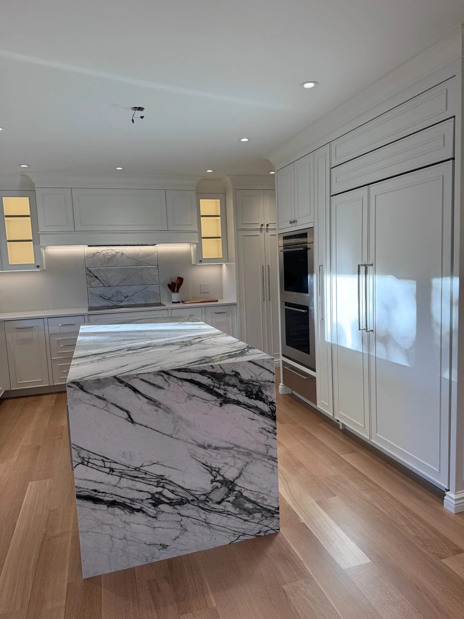 Modern kitchen with white cabinets, marble island, and wooden flooring.