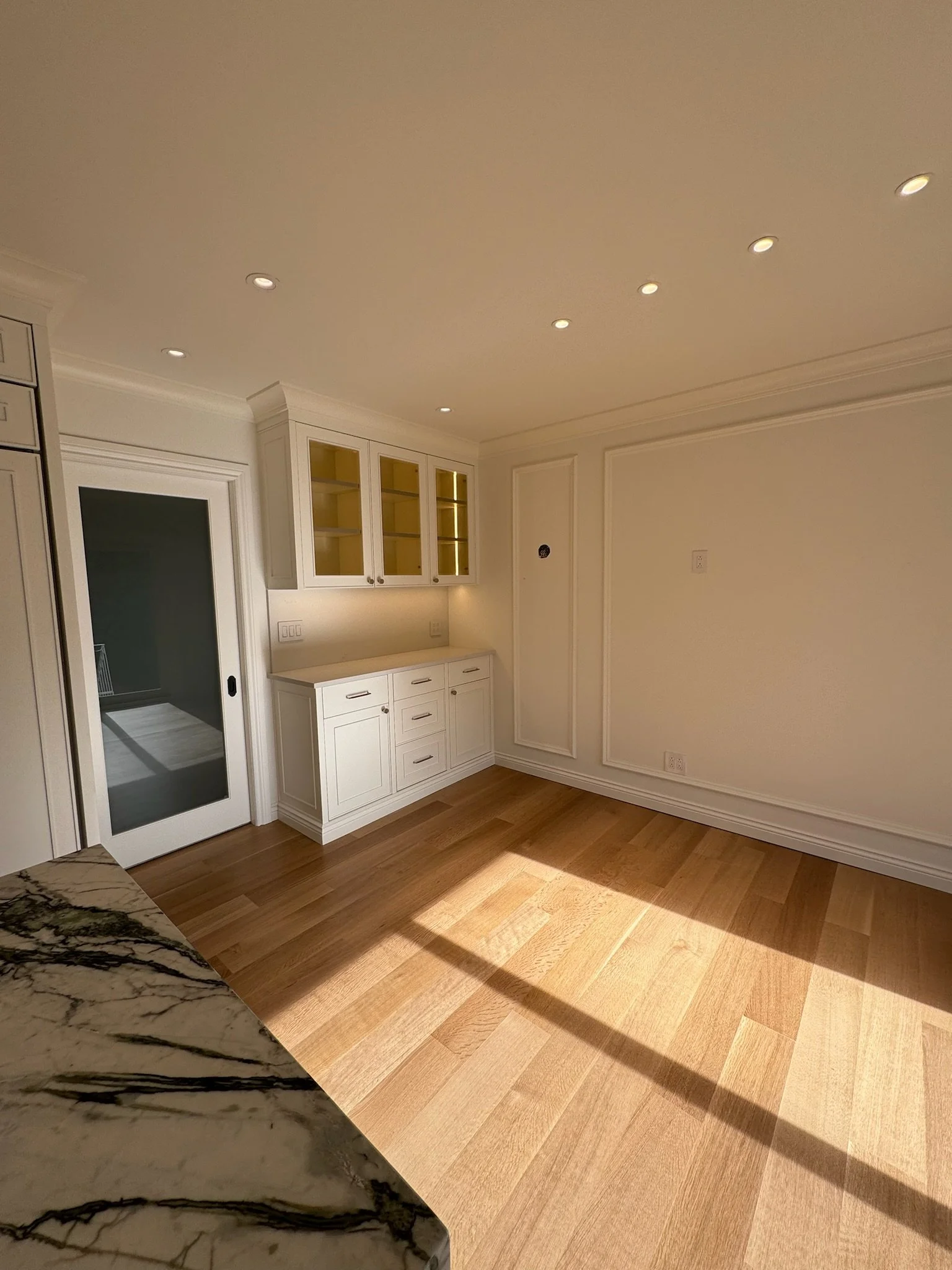Interior view of a room with white cabinets, wood flooring, and a marble countertop in the foreground.