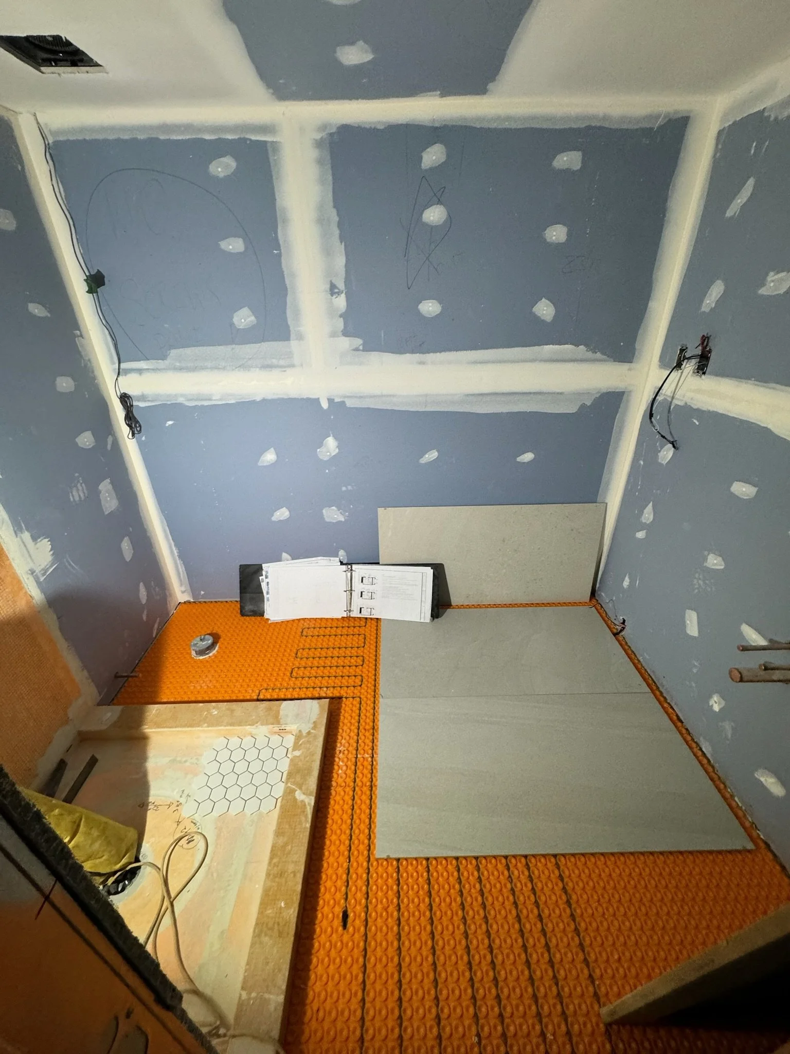 Underside of a construction or renovation space with drywall, electrical wires, and an orange anti-slip mat on the floor.