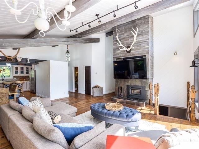 Living room with a gray sectional sofa, blue ottoman, wooden fireplace, mounted TV, antler decor, and rustic wood accents.