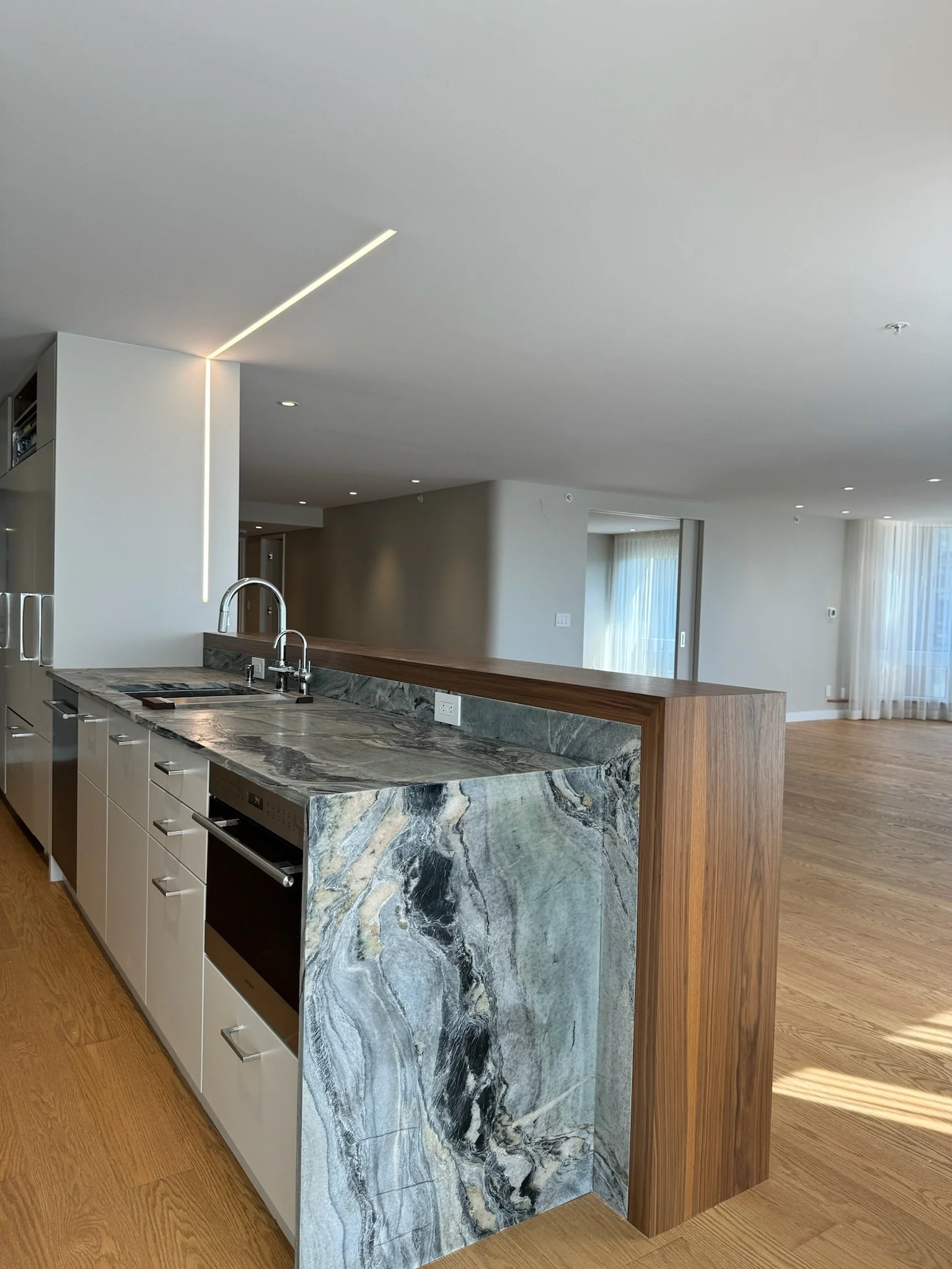 Modern kitchen with a marble island, stainless steel appliances, and hardwood flooring, spacious living area with large windows and curtains.
