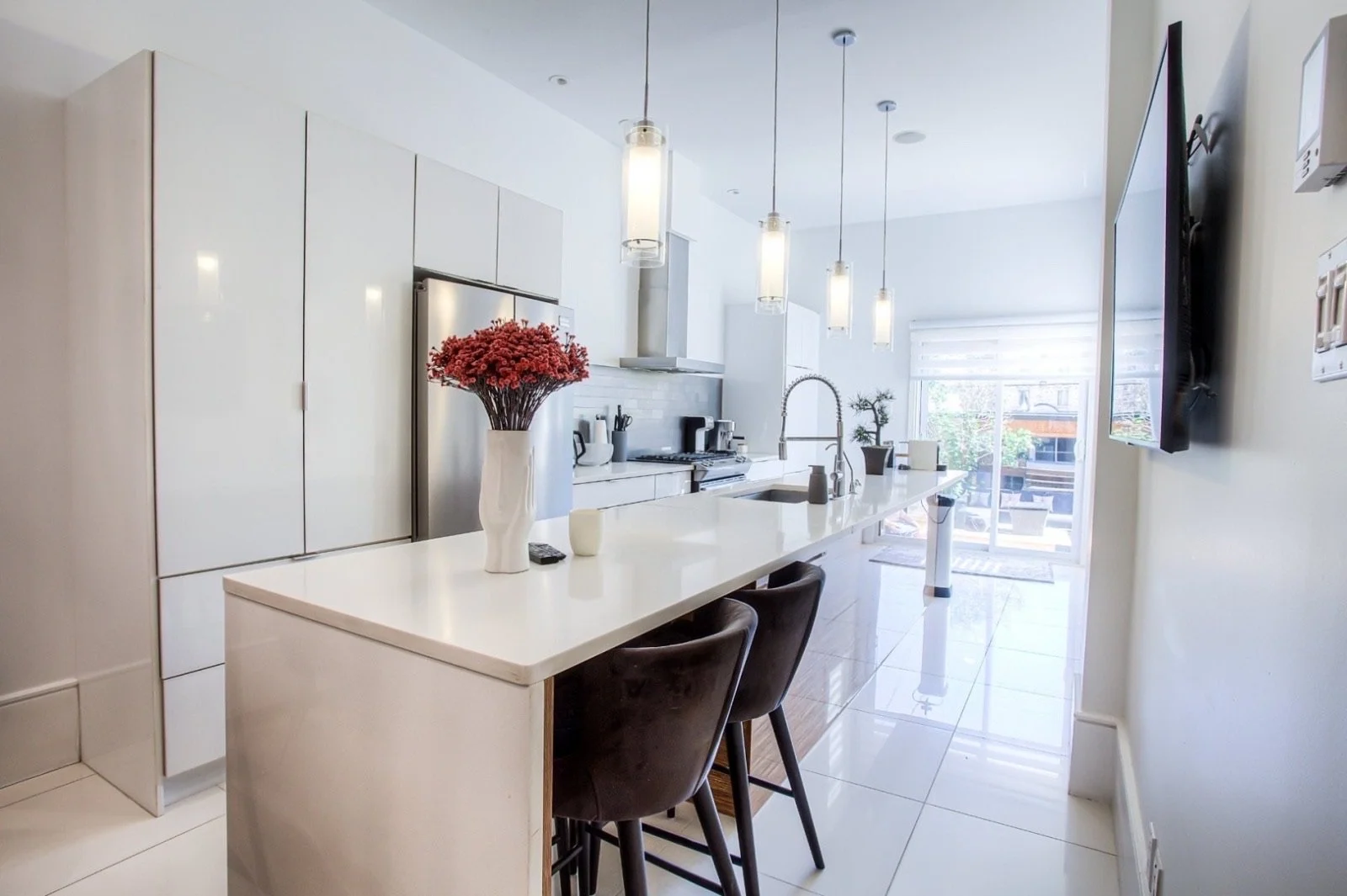 Modern white kitchen with island, black chairs, and pendant lights.
