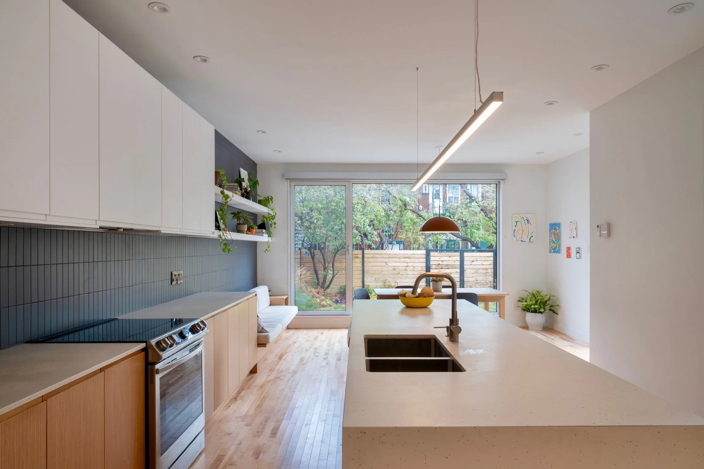 Modern kitchen with white cabinets, black stove, wood flooring, large window with outdoor view, pendant light, and art on the walls.