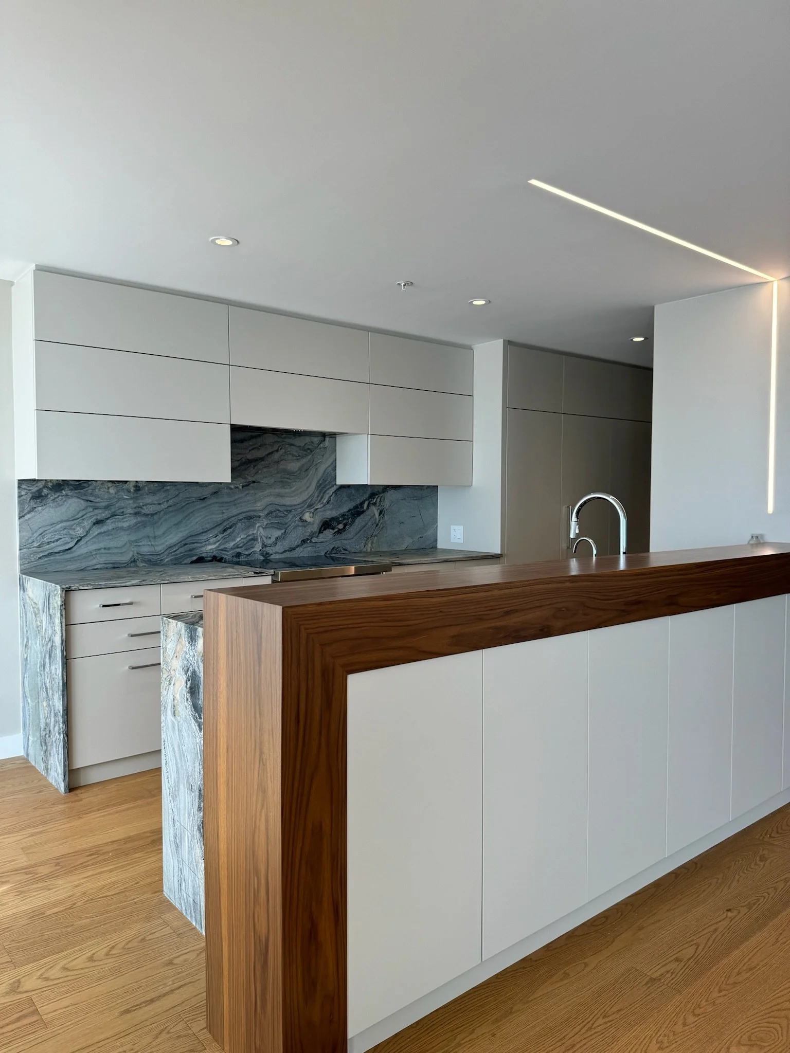 Modern kitchen with white cabinets, a marble backsplash, a wooden kitchen island, hardwood flooring, and ceiling lights.