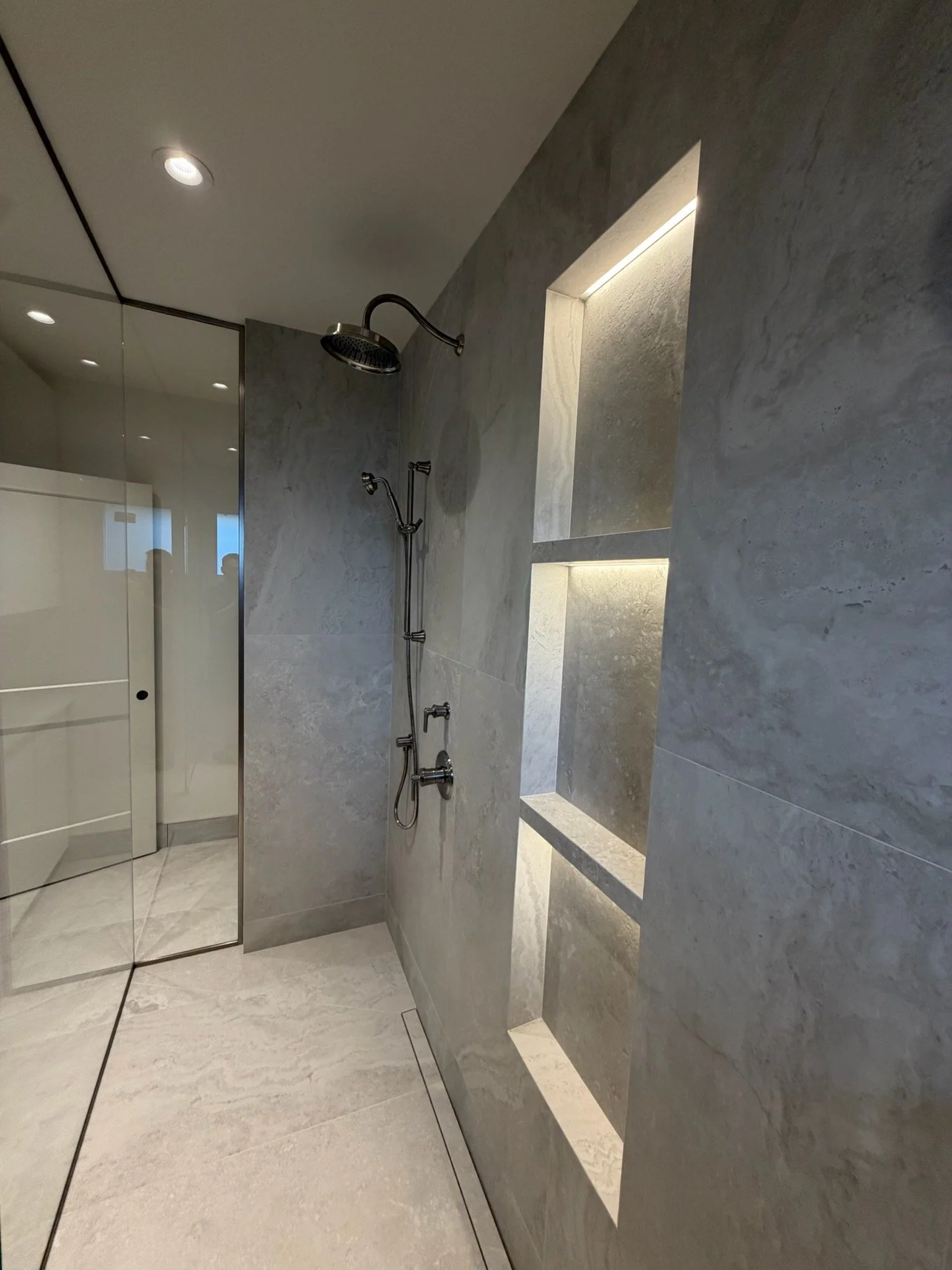 Modern shower area with gray marble walls, a built-in niche for toiletries, and a rainfall showerhead.