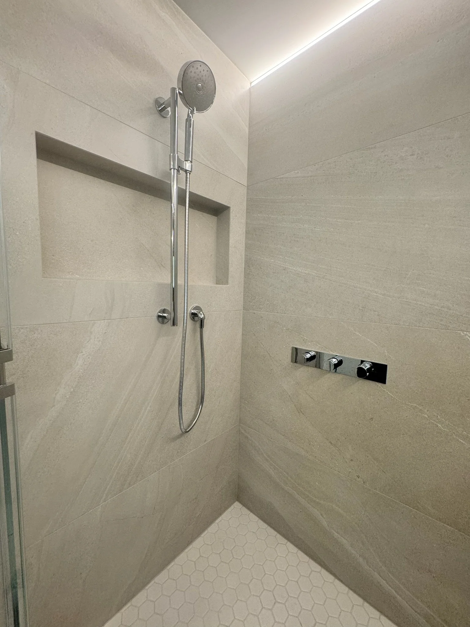 Modern shower with beige tiled walls, a chrome handheld showerhead, and a built-in shower niche.