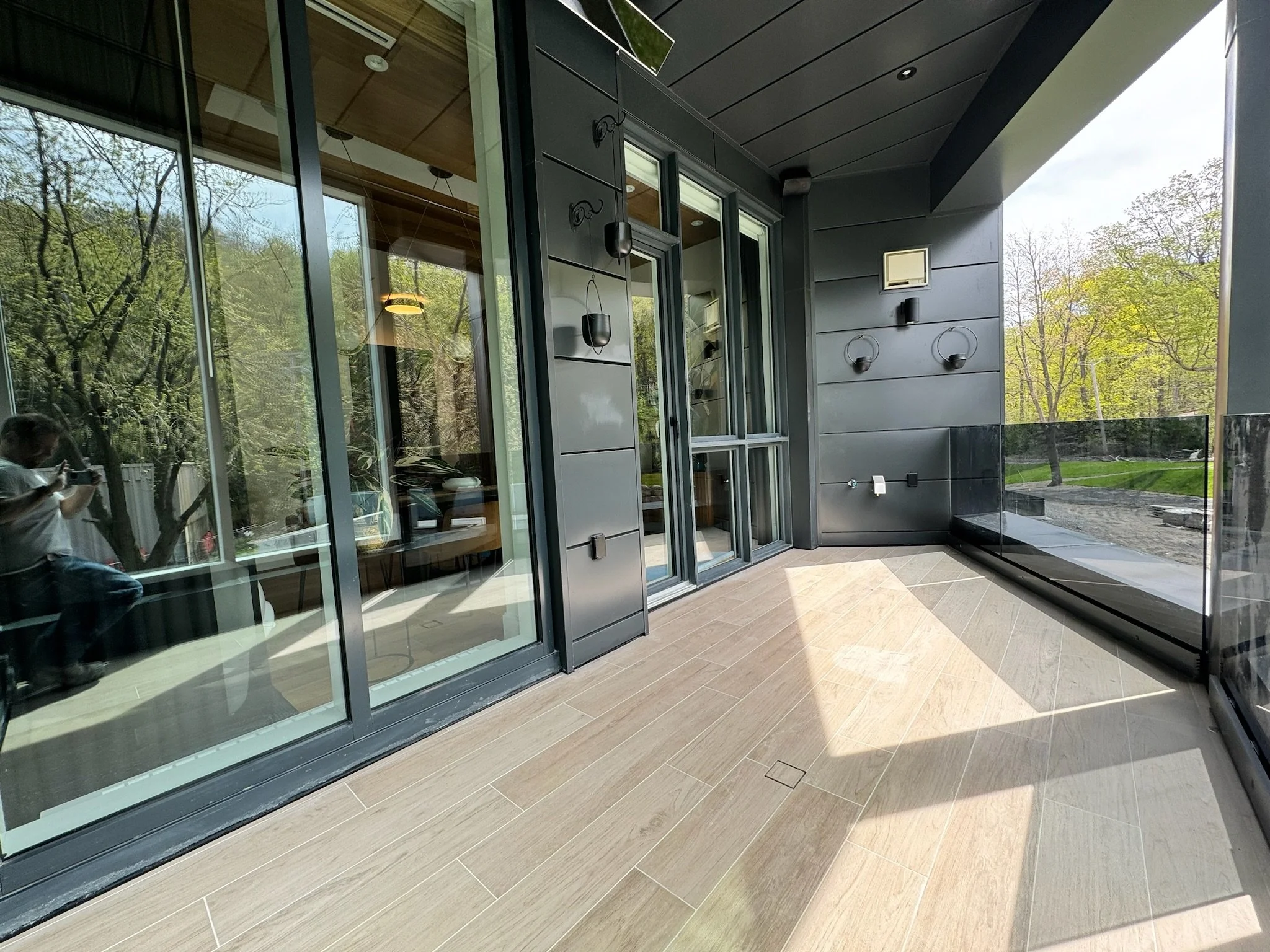 Modern building with large glass windows and black exterior panels, surrounded by trees and greenery.