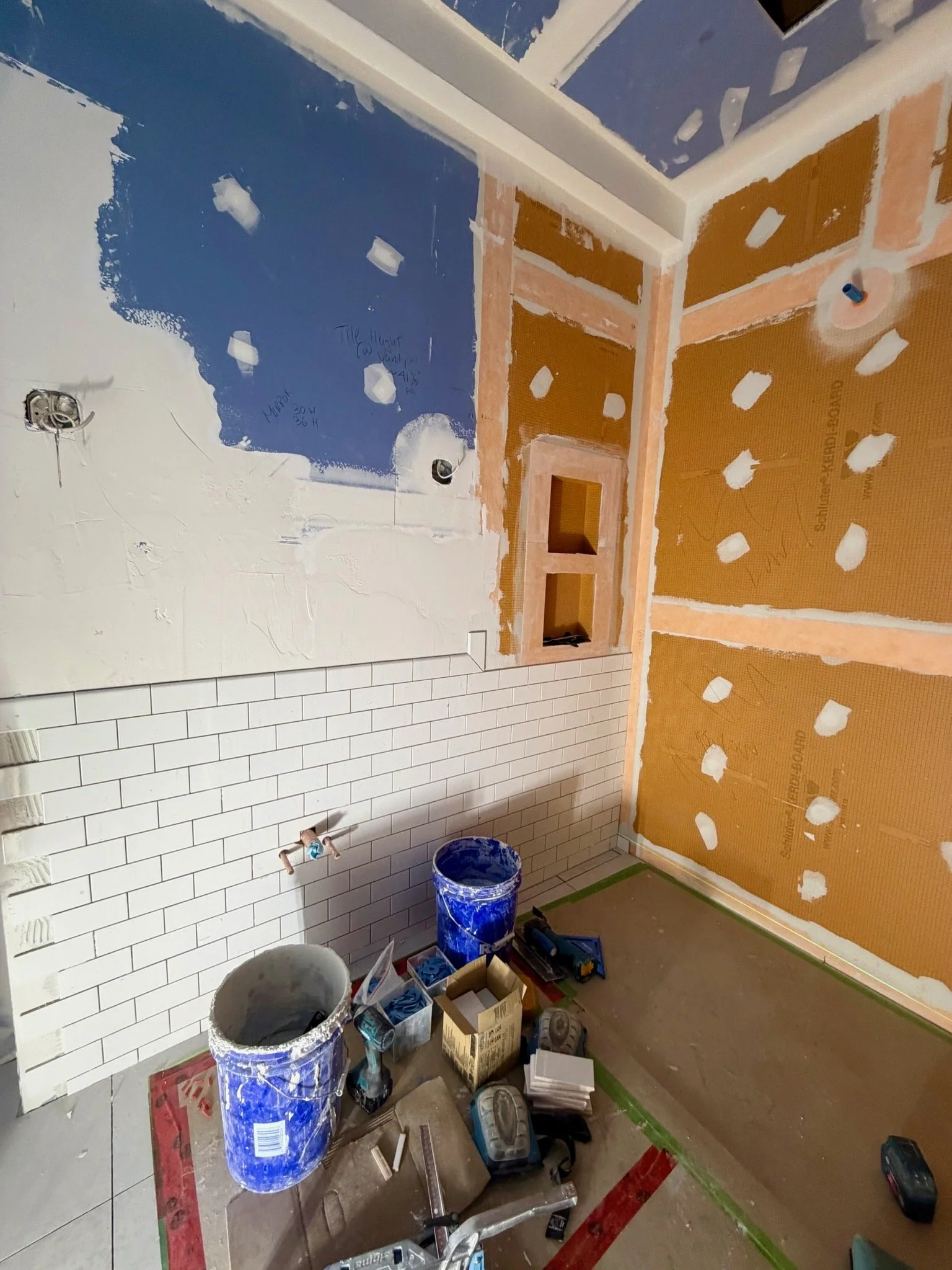 A room under construction with partially painted walls, tools, and construction supplies scattered on the floor.