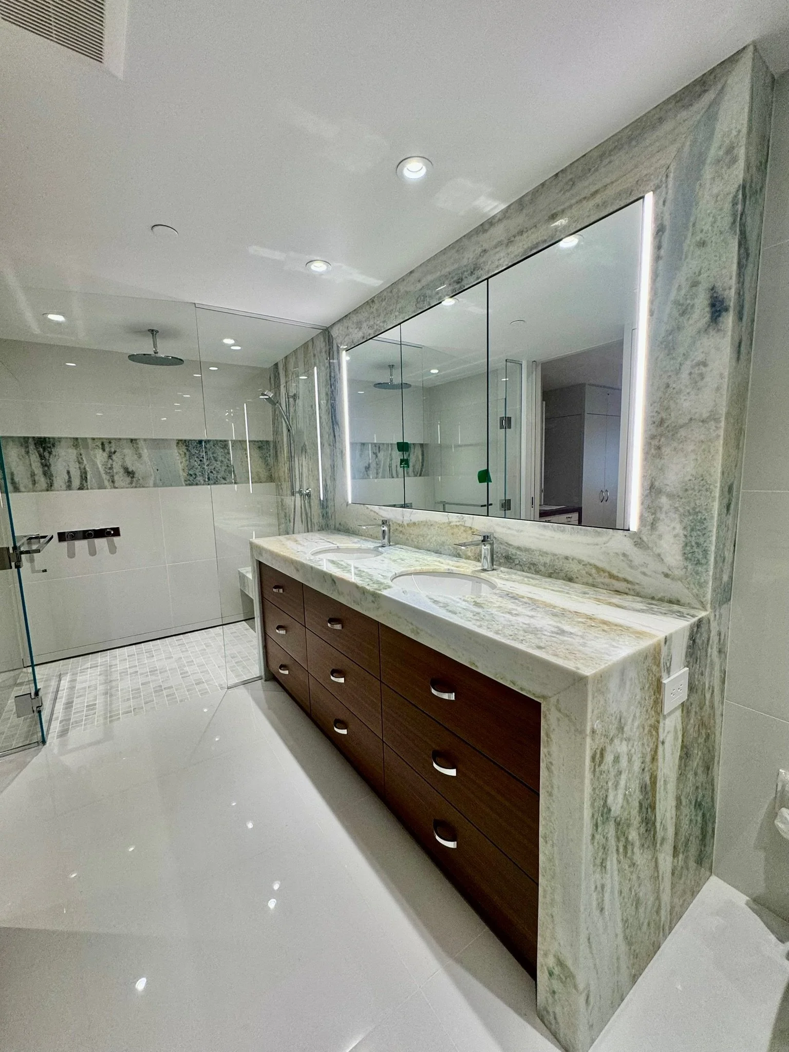 Modern bathroom featuring a double sink vanity with a marble countertop, a large rectangular mirror with LED lighting, and a walk-in shower with glass enclosure and rainfall showerhead.