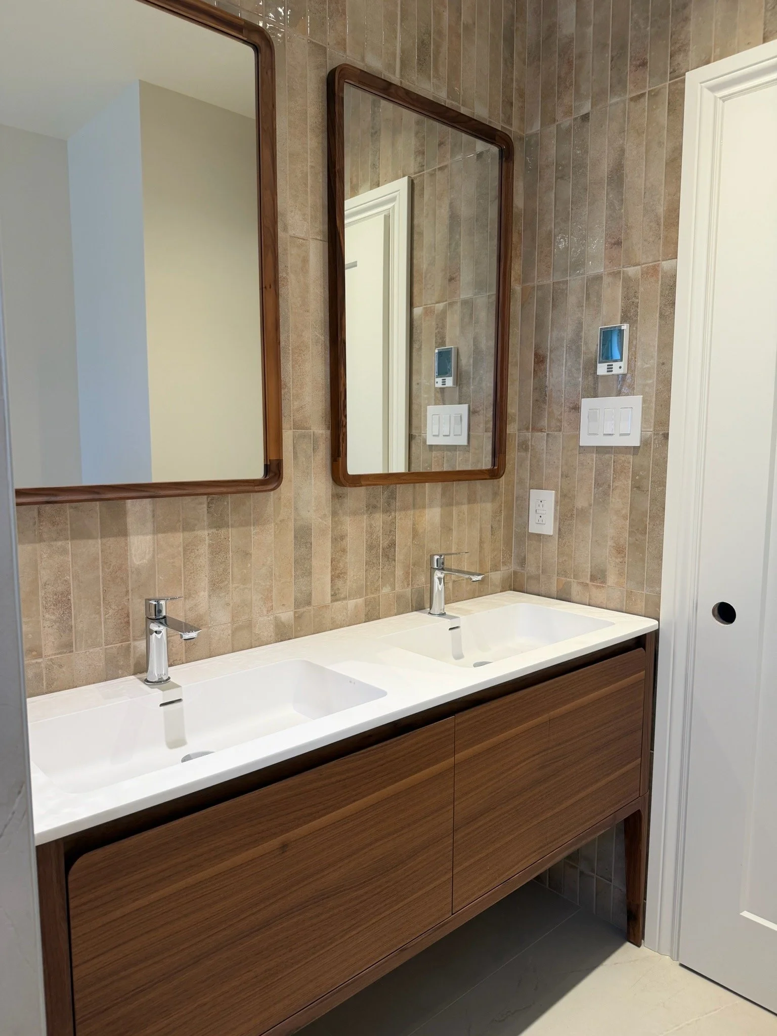 Double vanity bathroom with two rectangular mirrors, beige tiled wall, and a wooden cabinet with two sinks and modern silver faucets.