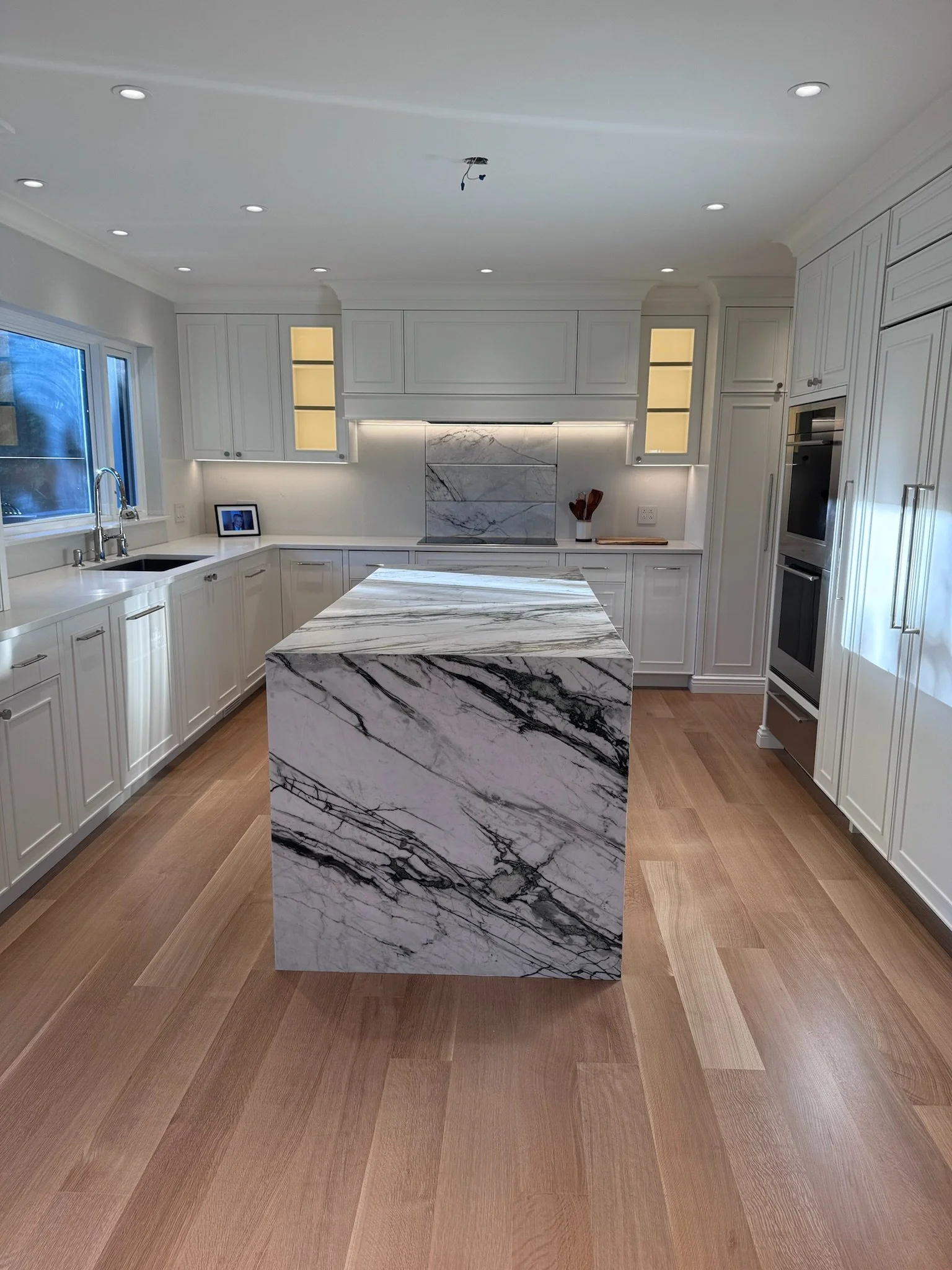 Kitchen with white cabinets, marble island, hardwood floor, and under-cabinet lighting.