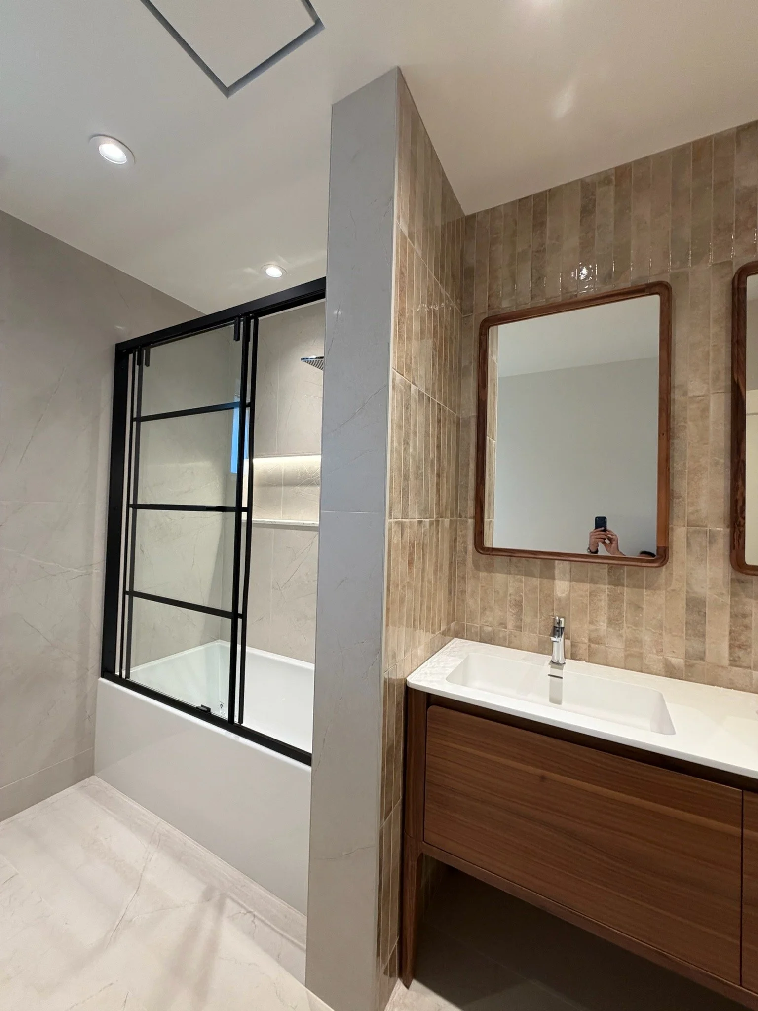 Modern bathroom with a shower enclosure, a vanity with a sink, and mirrors, featuring beige and brown tiled walls and a white marble floor.