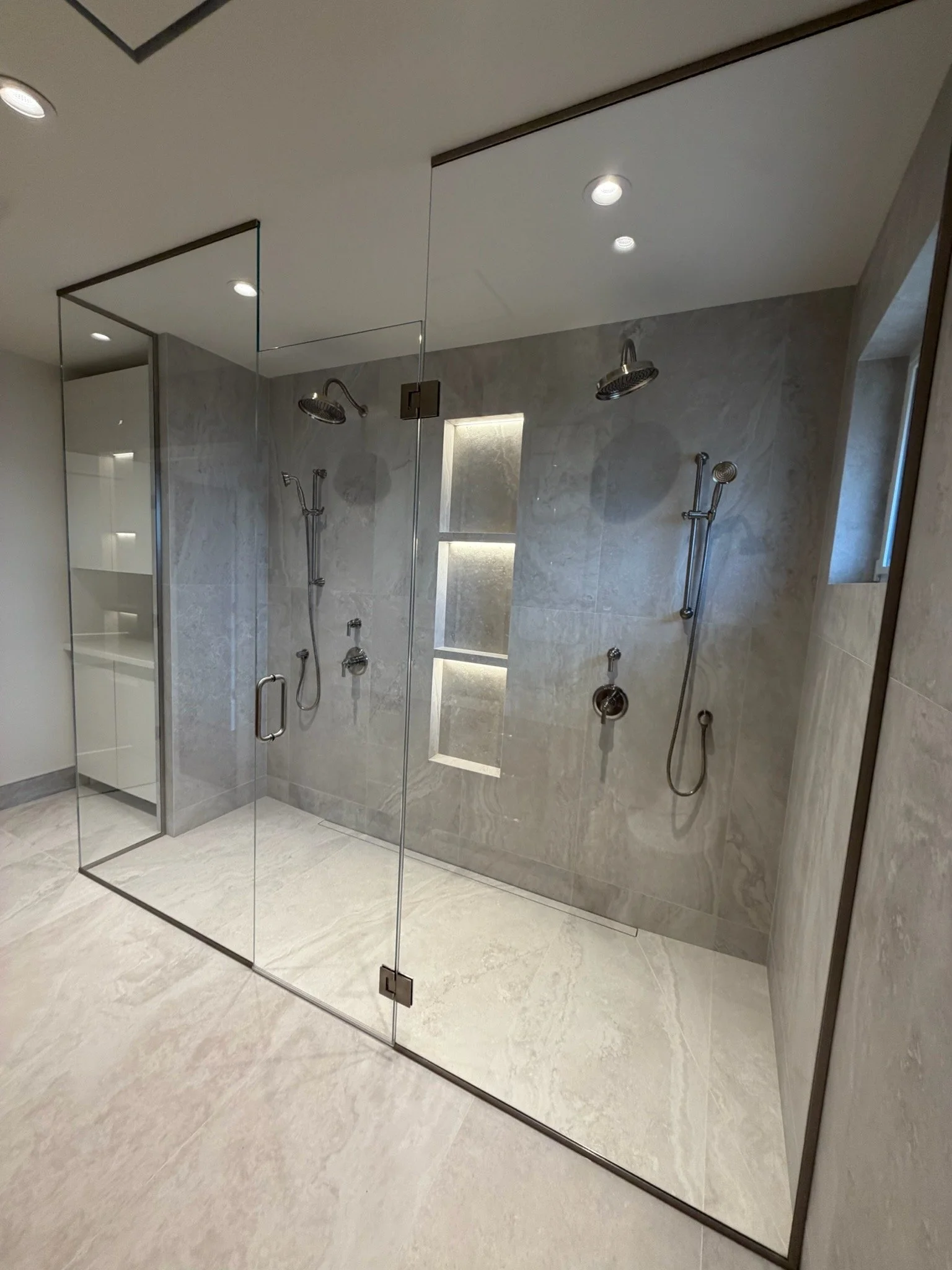 Modern bathroom with shower area enclosed by glass door, multiple showerheads, and built-in wall niches for storage.