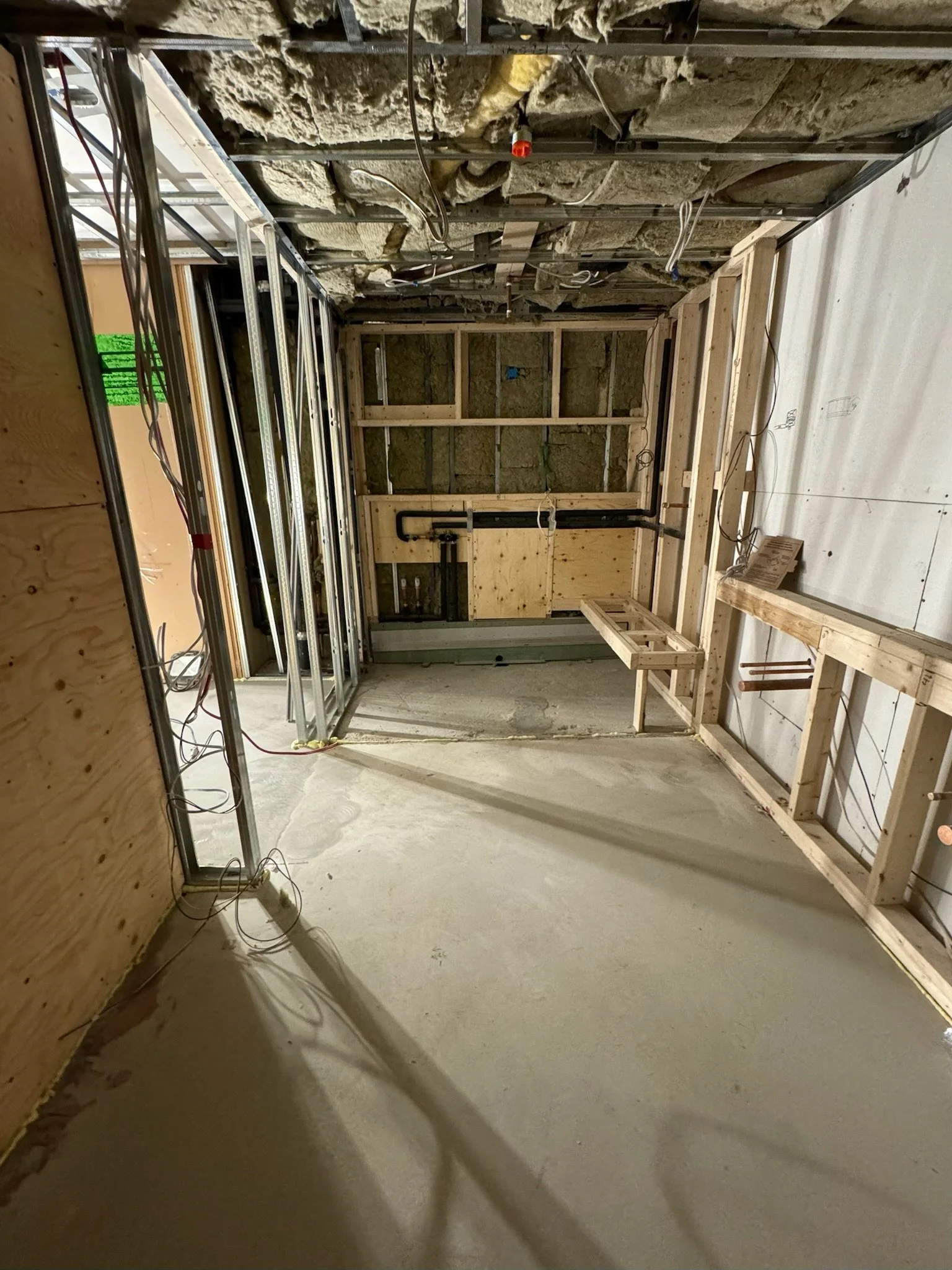 Interior of a building under construction with wooden framing, exposed insulation, and electrical wiring.