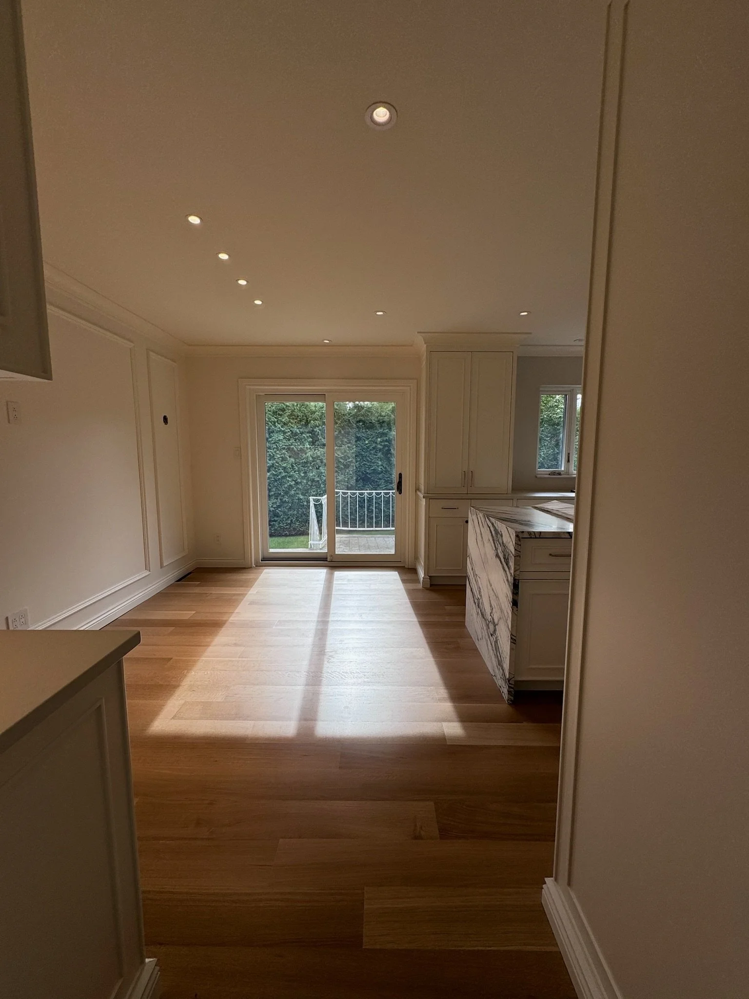 Modern kitchen with light wood flooring, white cabinets, a marble countertop, and a sliding glass door leading to an outdoor area.