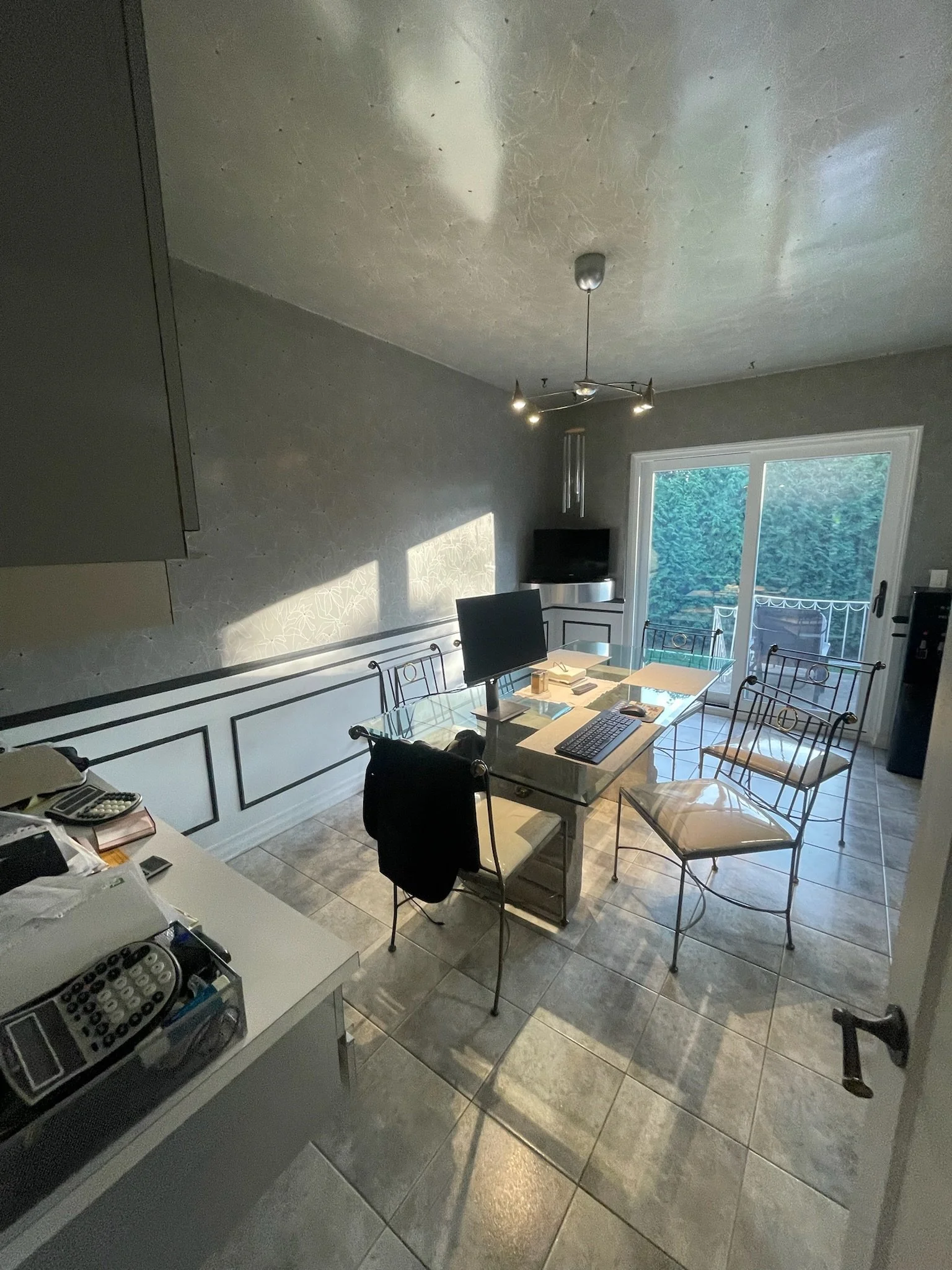 A dining room with a glass table surrounded by four chairs, a sliding glass door leading to a patio, a television, and a ceiling fan with lights.
