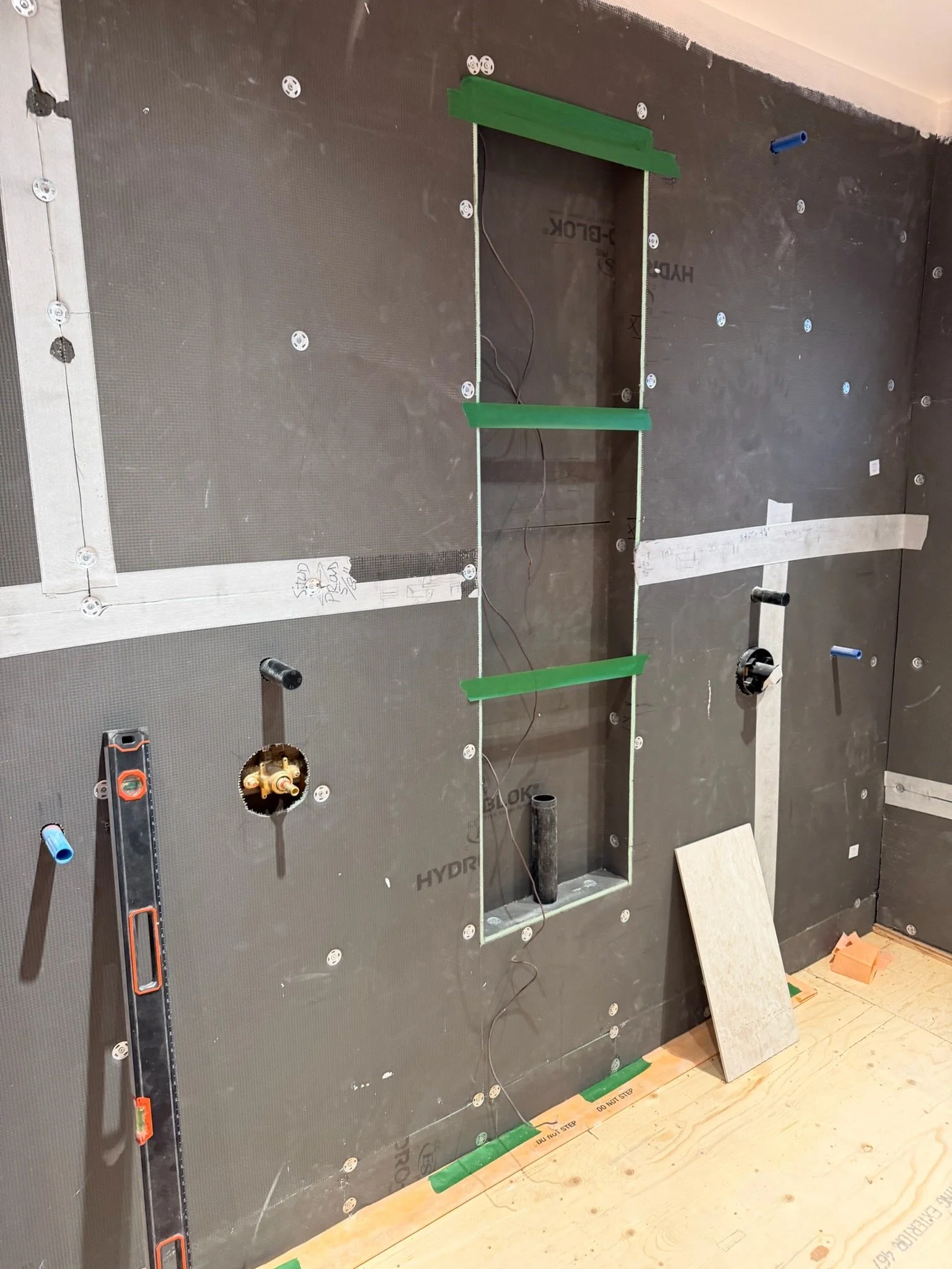 Construction wall with windows cutouts and insulation, tools, and wiring in progress, with green tape on the wall.