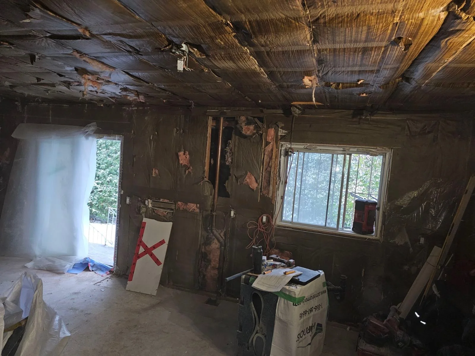 A room under renovation with insulation and exposed walls. There are two windows letting in natural light, construction tools, and materials scattered around.