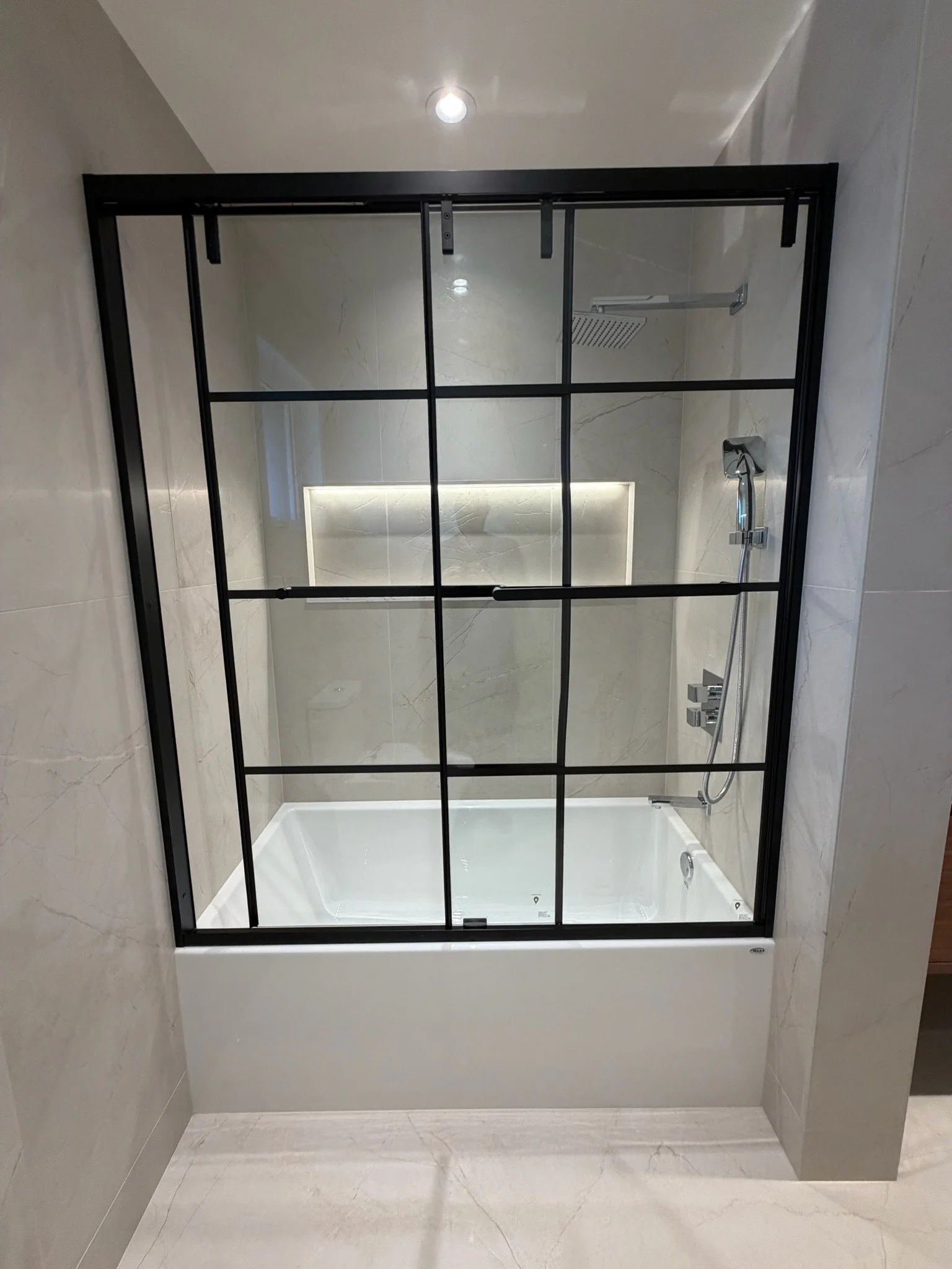 Modern walk-in shower with large glass enclosure, beige marble walls, rain shower head, and handheld shower fixture.