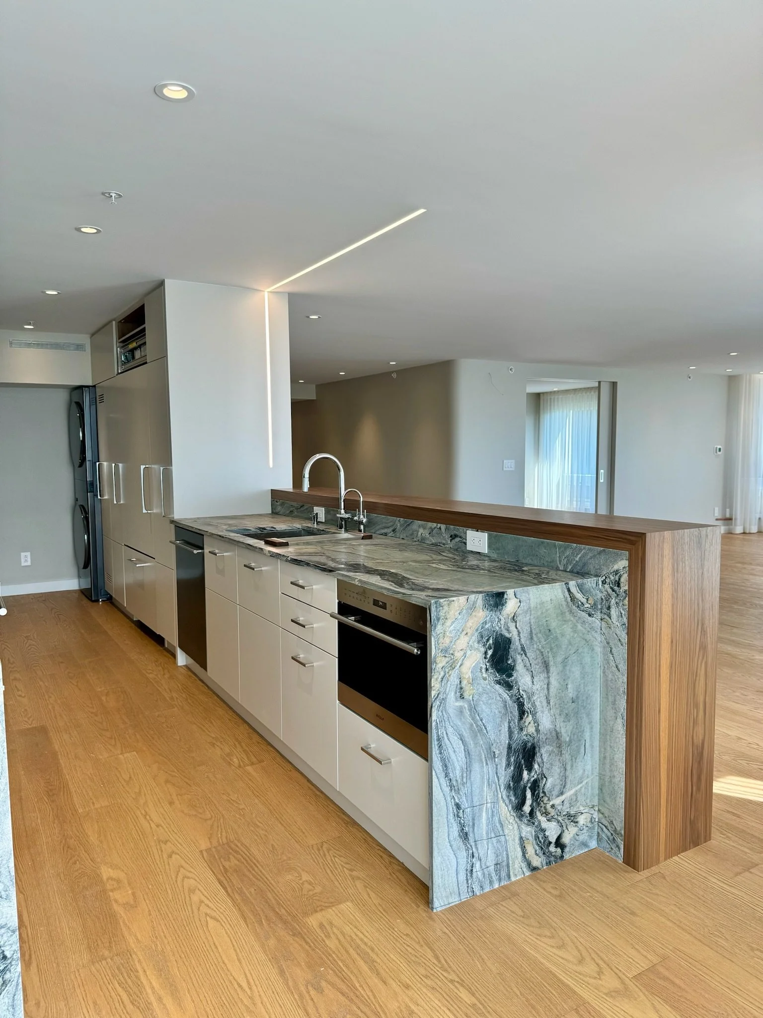 Modern kitchen with marble island, wooden accents, light wood flooring, and minimalist design.