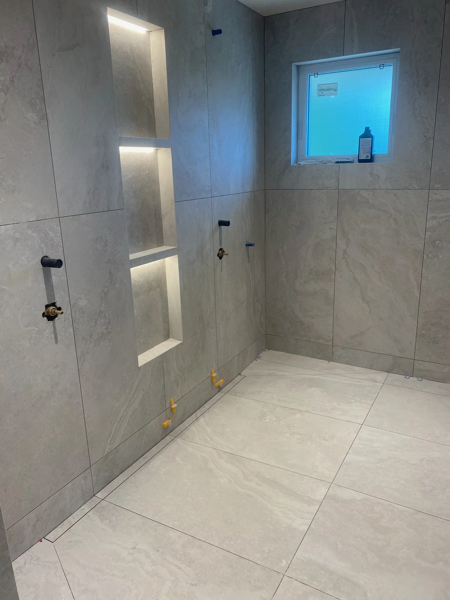 Bathroom or shower area under construction with empty wall niches, a small window with cleaning bottle, and floor tiles.