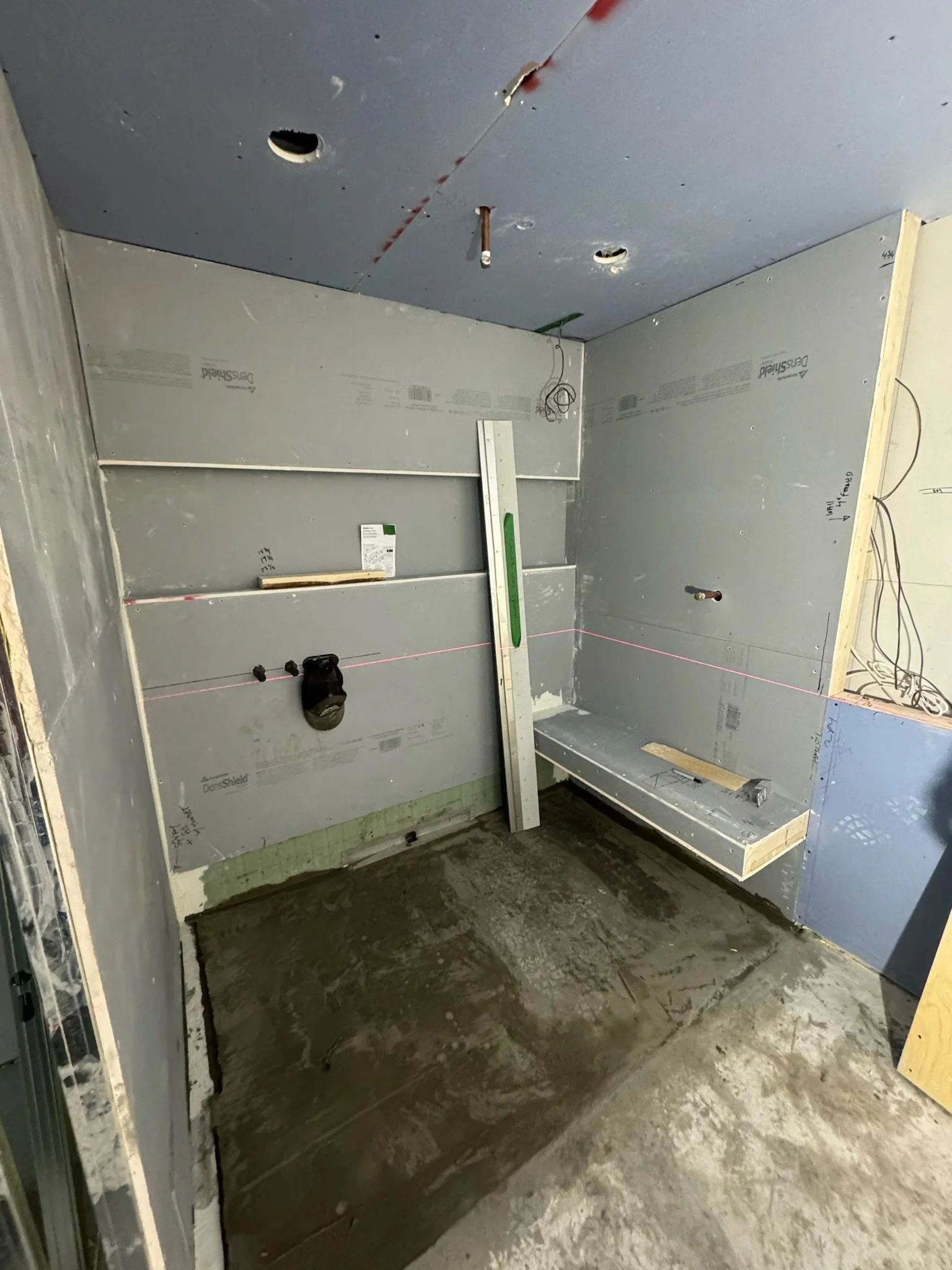 Interior of a room under construction with drywall installed, electrical wiring visible, and a concrete floor.