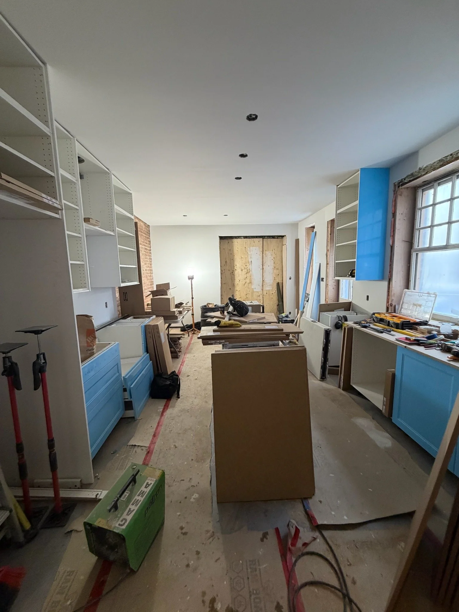 Interior of a room under renovation with white shelving units, tools, construction materials, and partially finished walls.