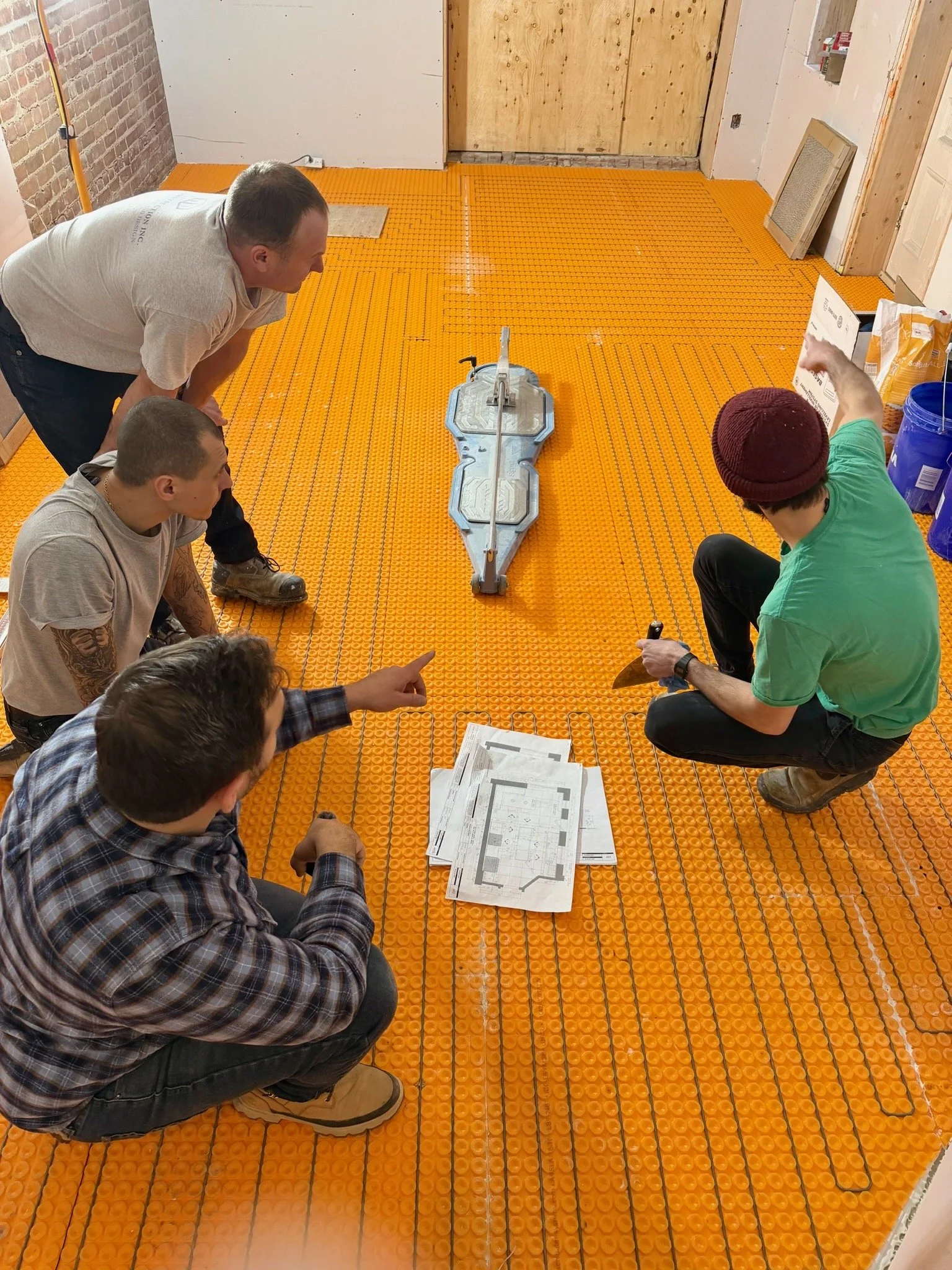 People working on a floor installation with orange interlocking floor tiles, blueprints, and construction tools.