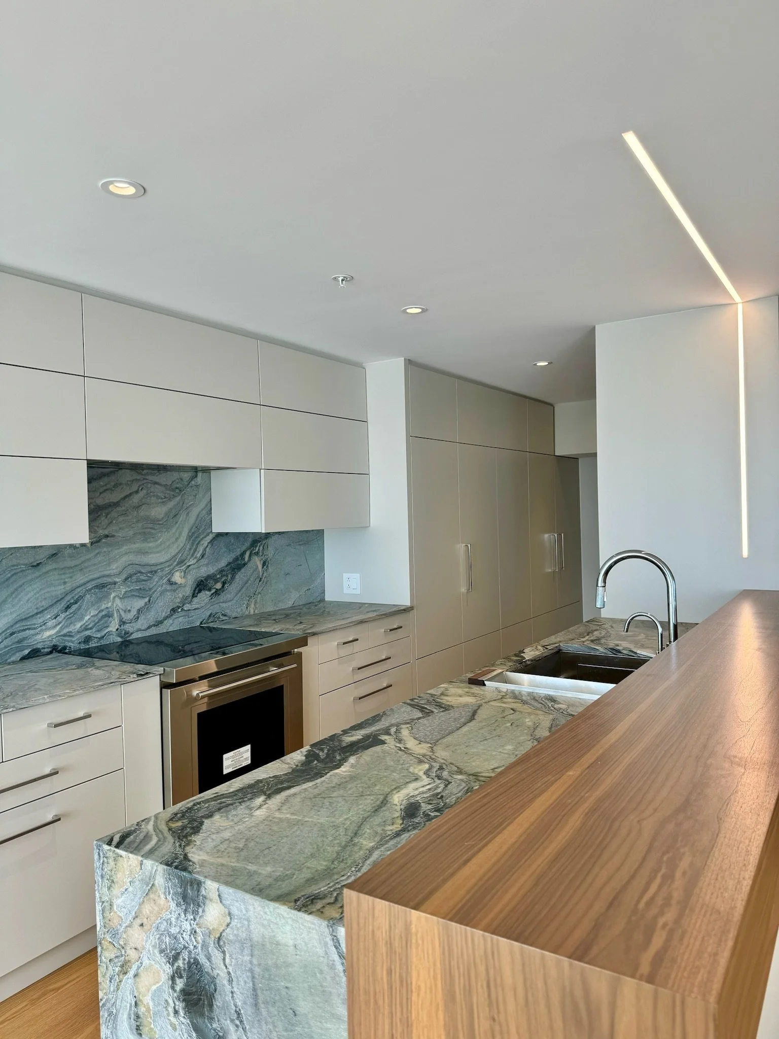 Modern kitchen with marble countertops, beige cabinets, stainless steel appliances, and a wooden island.