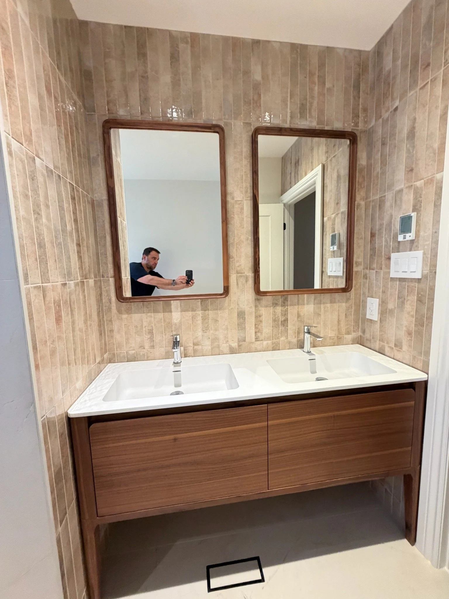 A bathroom vanity with two sinks and mirrors above, set against a tiled beige wall.