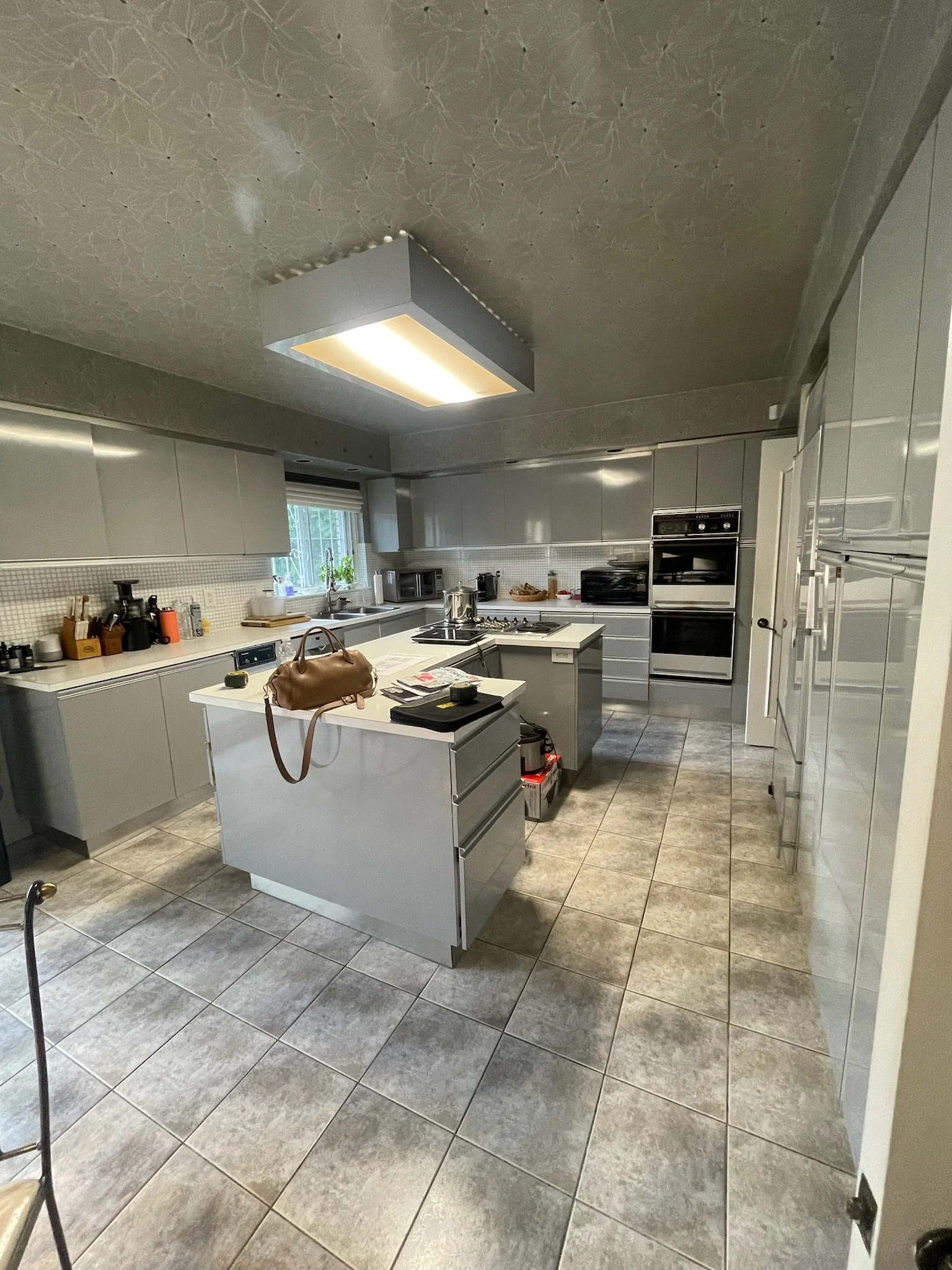 A modern kitchen with gray cabinets, a kitchen island, stainless steel appliances, and tiled floors.