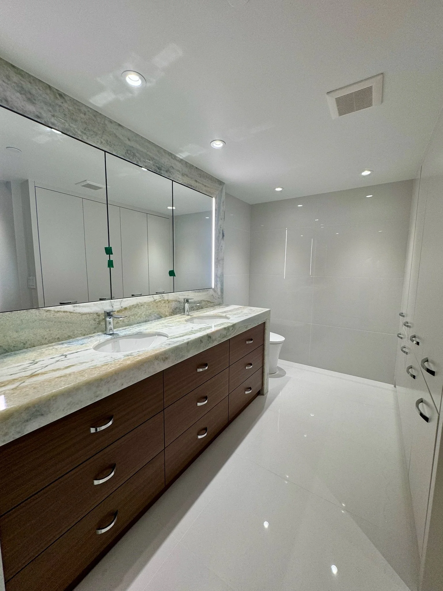 Modern bathroom with a double sink vanity, large mirror, white walls, white tiled floor, and ceiling lights.