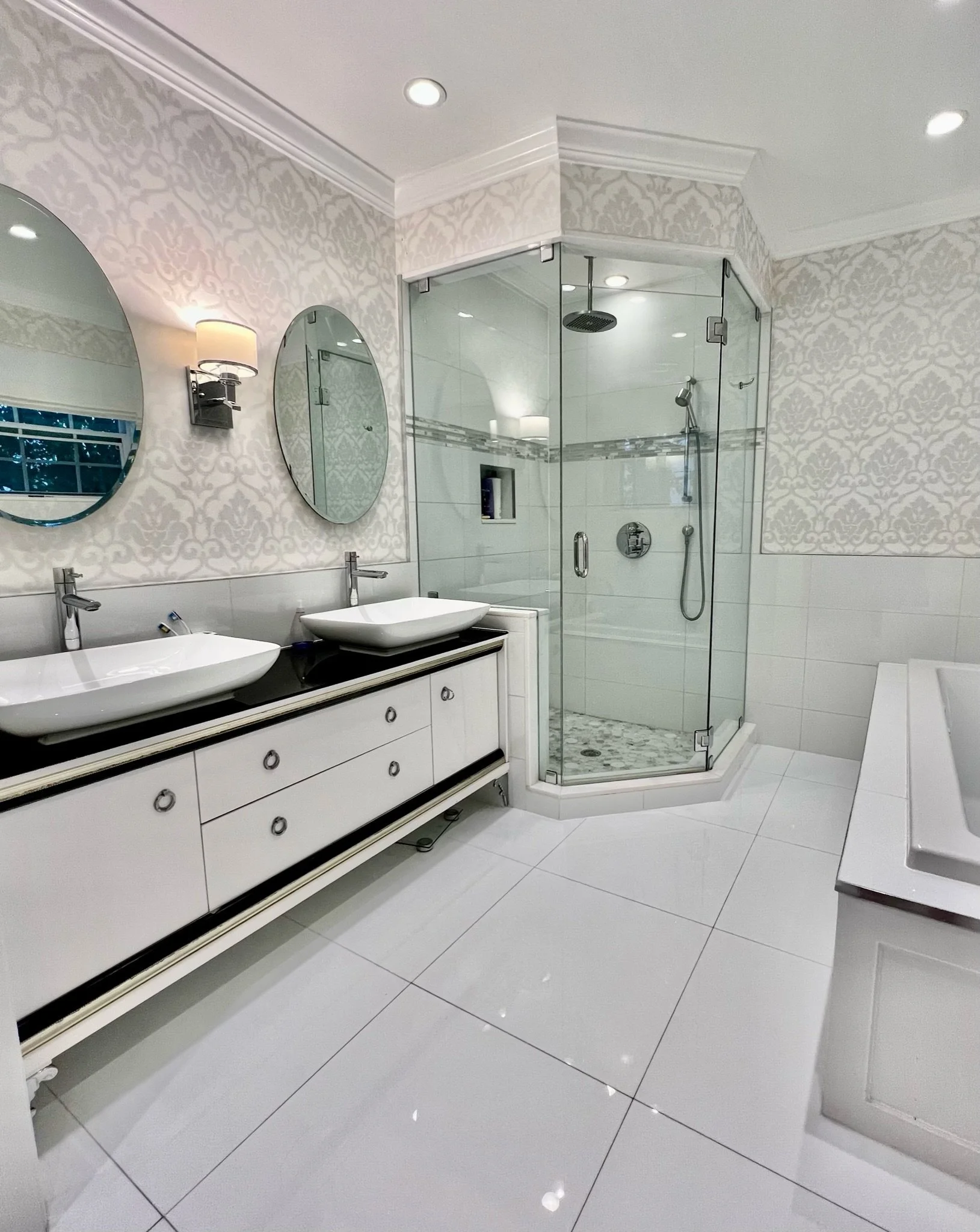 Modern bathroom with white tiled floors, a dual-sink vanity with round mirrors, a shower with glass doors, and decorative wallpaper.