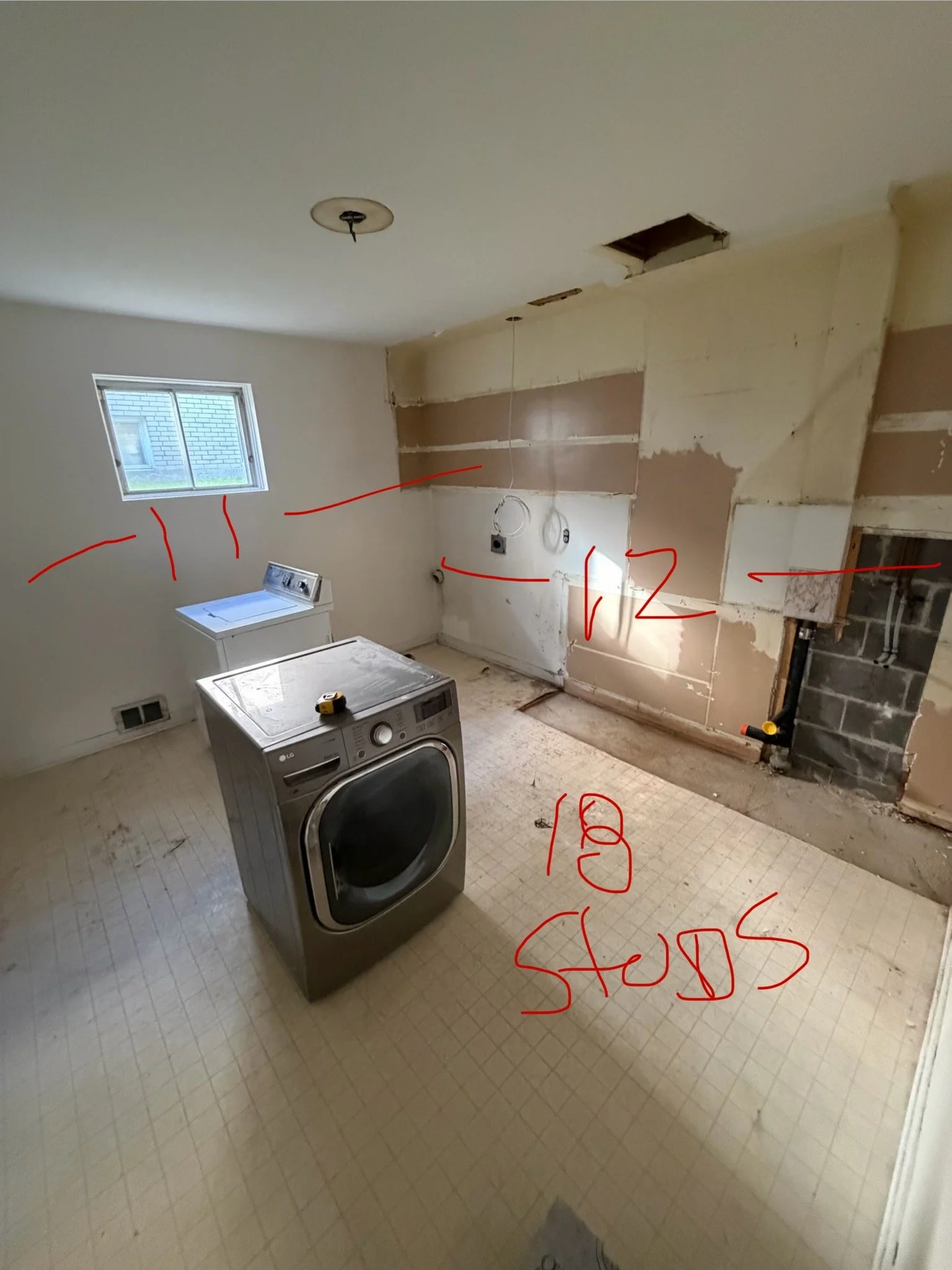 Kitchen undergoing renovation with exposed walls, a window, a washing machine, and construction markings and notes on the walls and floor.