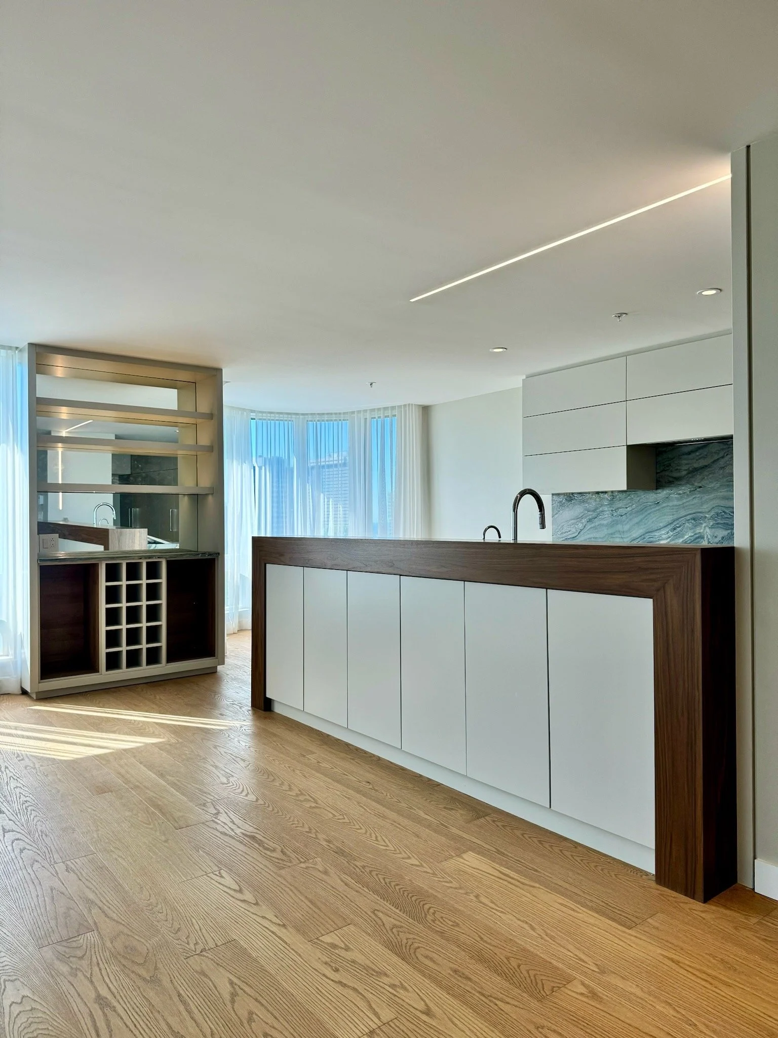 Modern kitchen with white cabinets, marble backsplash, wooden accents, and a curved bay window with curtains.