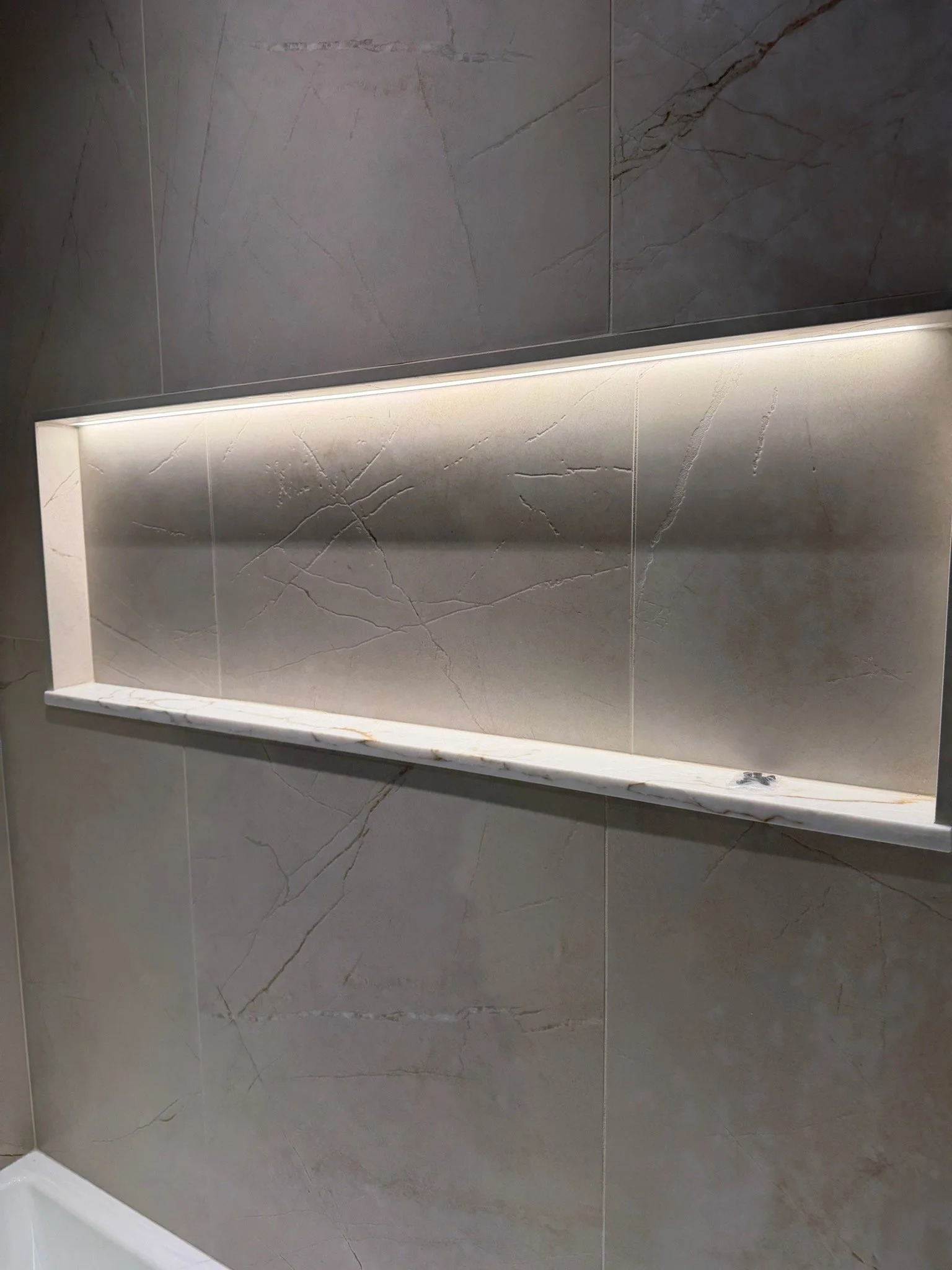 Close-up of a gray marble wall with a built-in shelf and strip lighting above it.