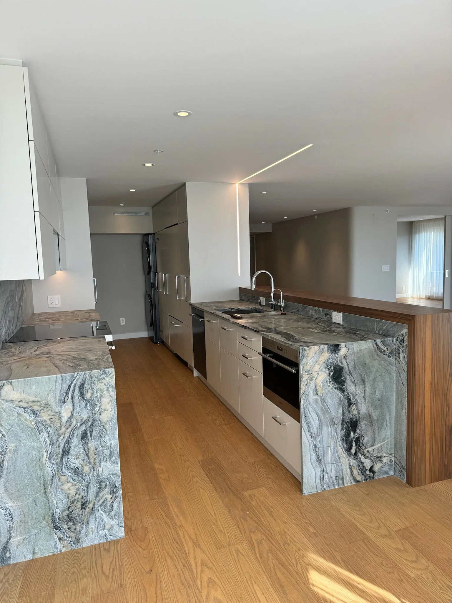 Modern kitchen with marble countertops, stainless steel appliances, wooden floors, and white cabinetry.
