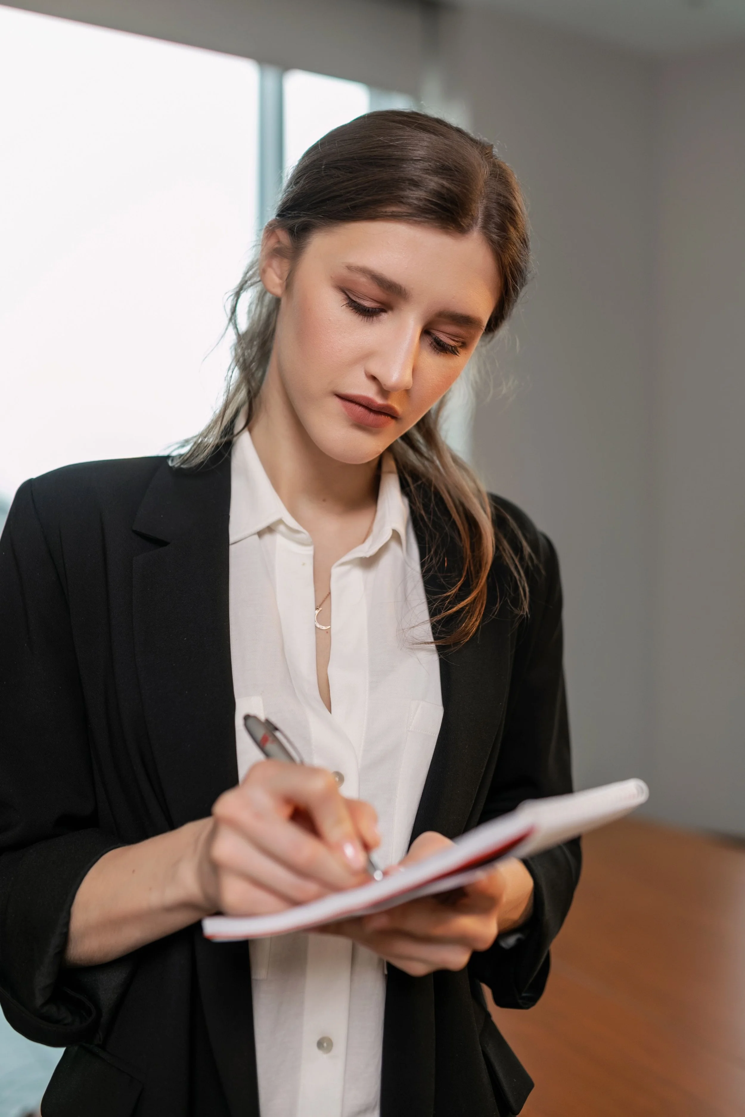 A woman in business attire writing in a notepad.