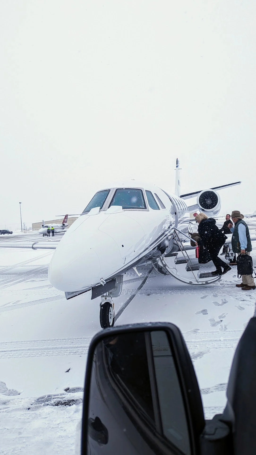 Private jet on snowy tarmac with people boarding, snow falling, and more aircraft in background. Steamboat Springs private jet tarmac pickup.