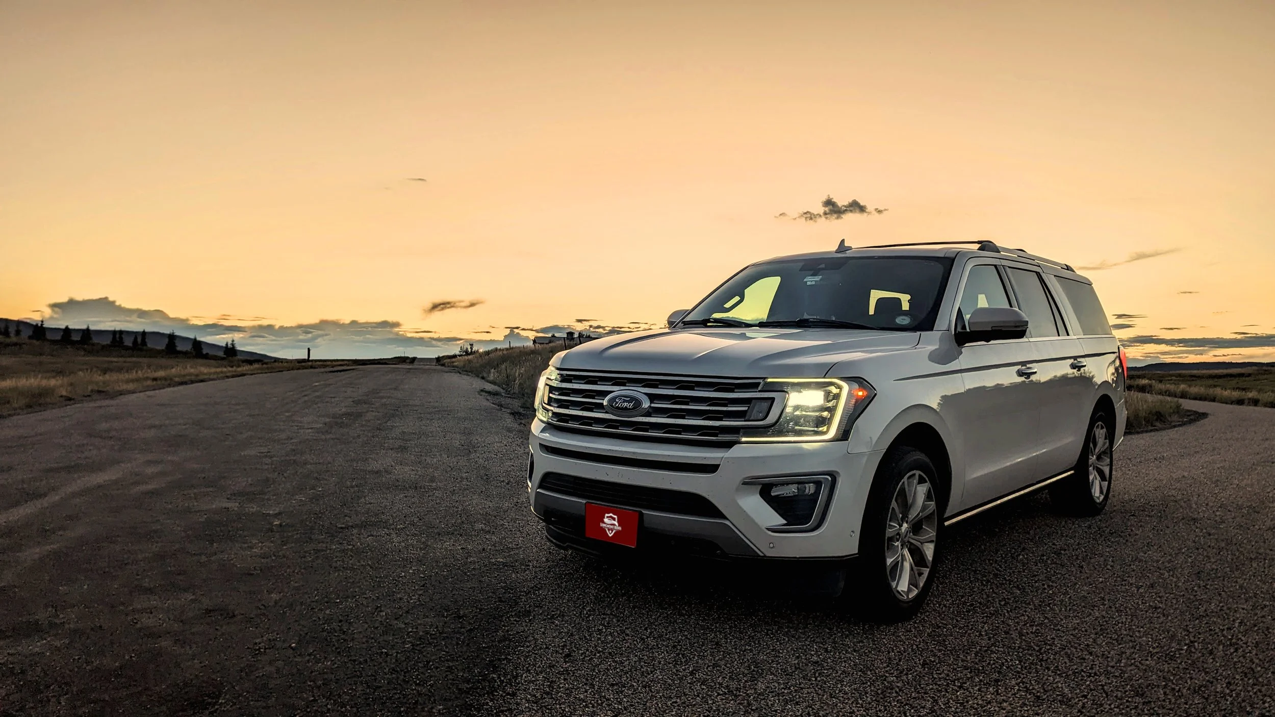 A white Ford SUV parked on the side of a deserted road during sunset, with a landscape of hills and trees in the background.