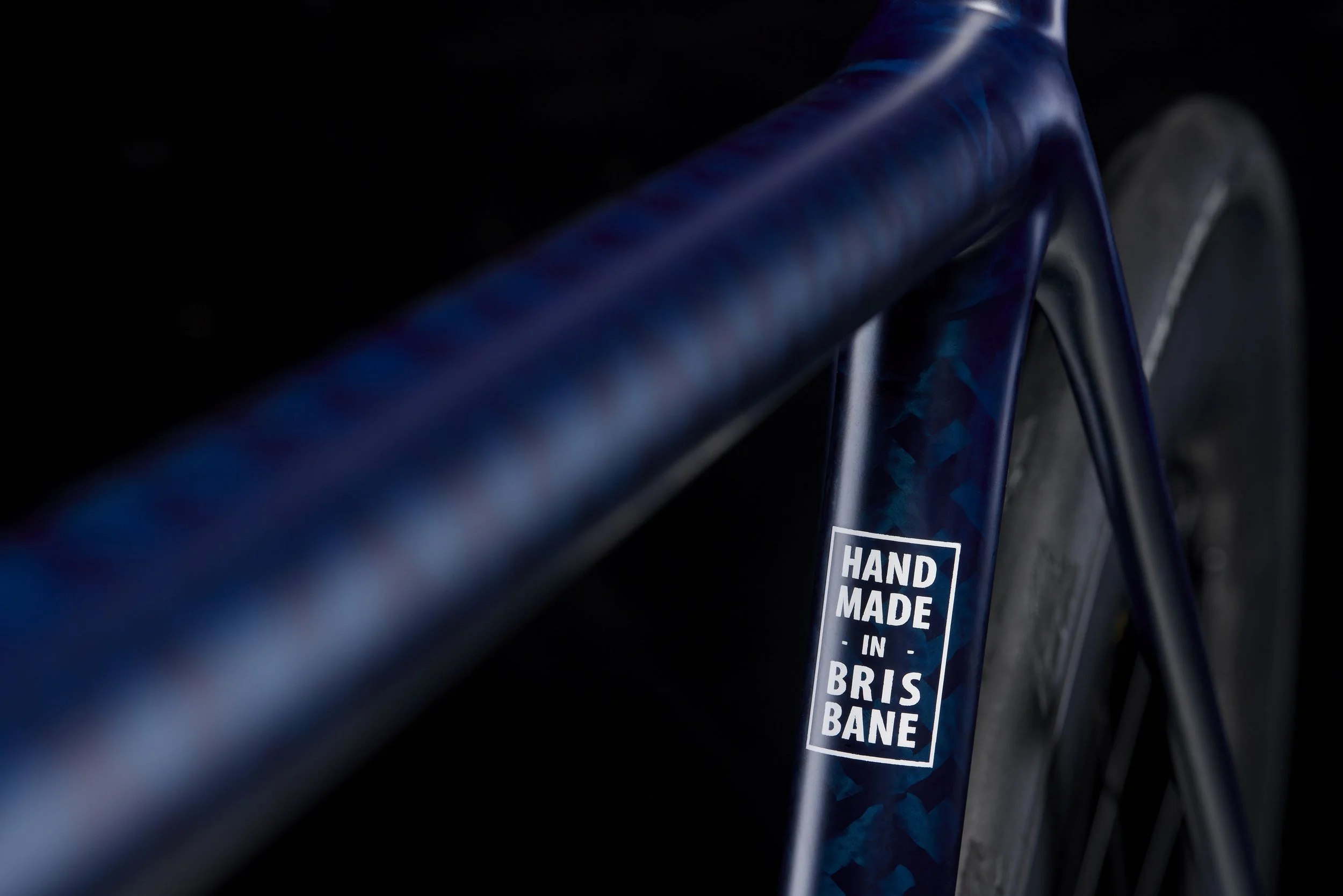 the words "made in Brisbane" painted on the blue down tube of a bicycle on a black background