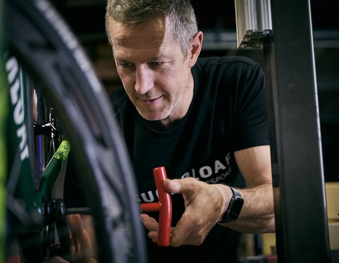close up image of man assembling a bicycle in a workshop with red tool in his hand