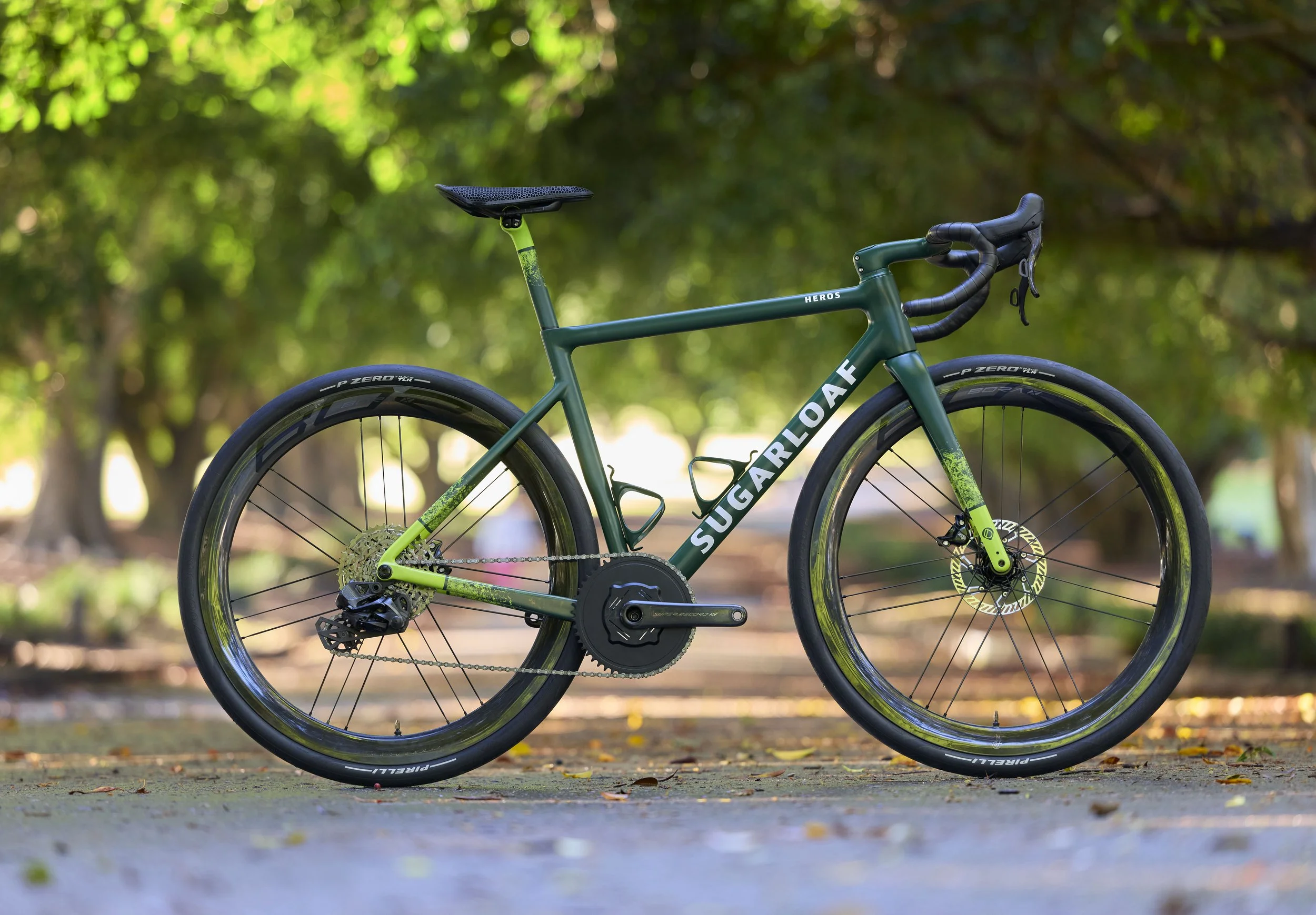 Green and Sugarloafcarbon road bike on a park path with trees in the background.