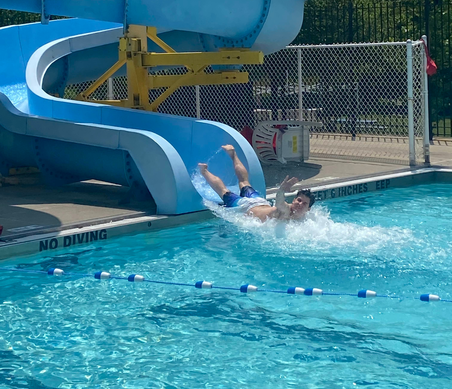 A person sliding off a blue water slide into a swimming pool.