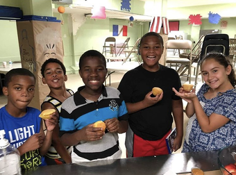 Five children smiling and holding cupcakes in a classroom or community center.