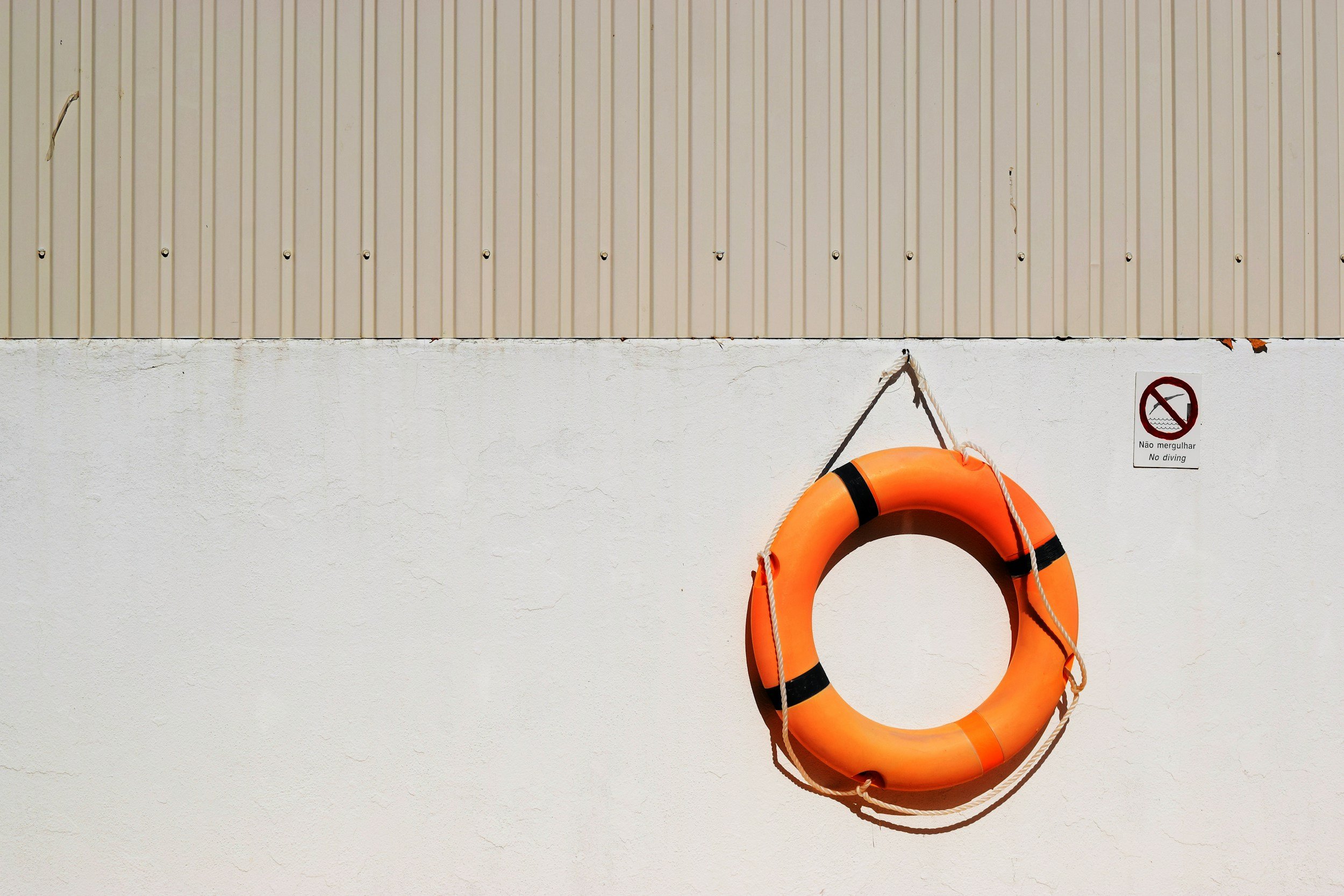 Orange life preserver hanging on a white wall with a small sign that reads 'No diving' in both Portuguese and English.