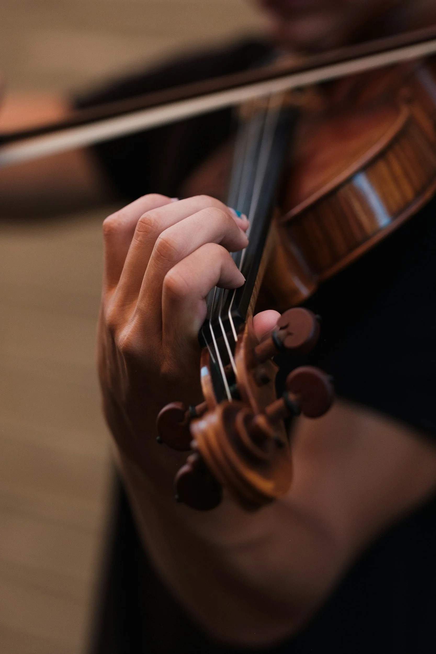 Close-up of a person’s hand playing a wooden violin, focusing on the fingers on the fingerboard.