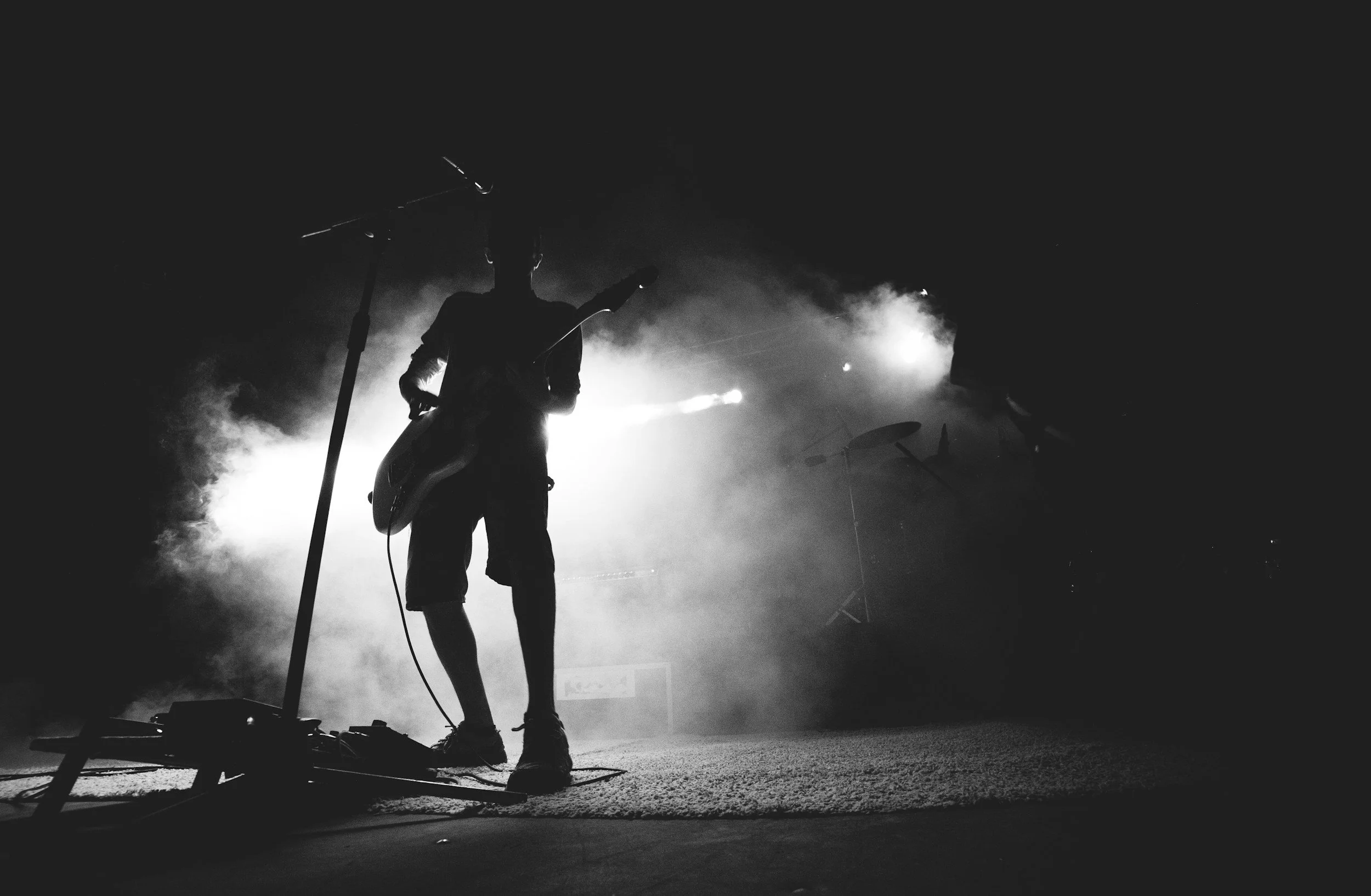 Silhouette of a person with a guitar on stage with fog and bright lights in the background.