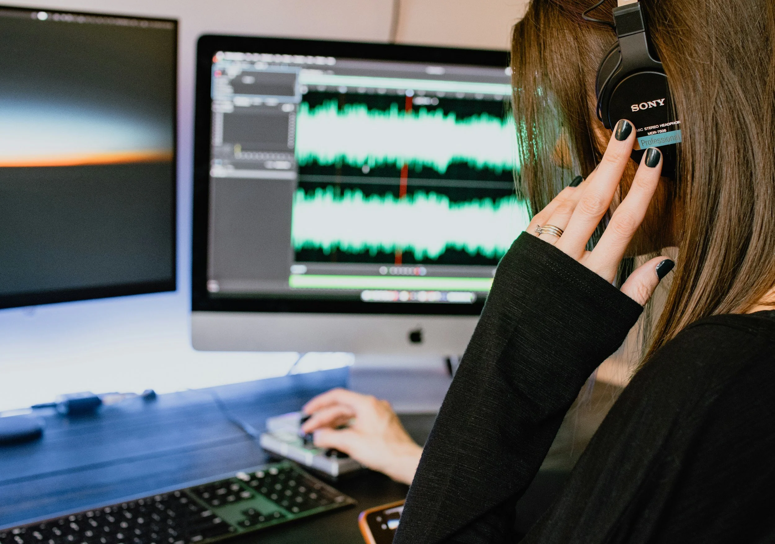 Woman wearing headphones using a computer with audio editing software on the screen.